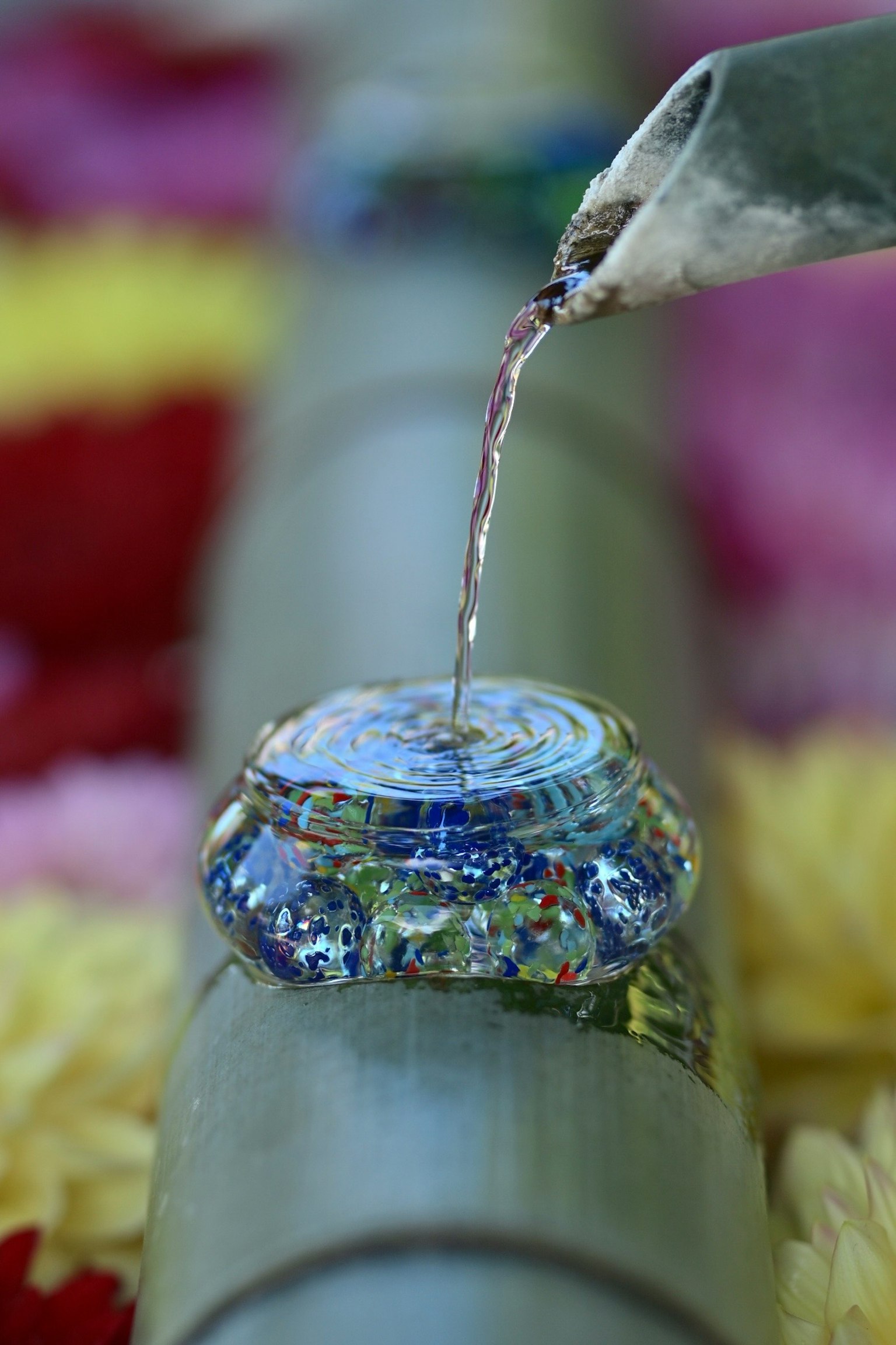 Acqua che scorre da un bambù in una ciotola di vetro decorativa circondata da petali di fiori