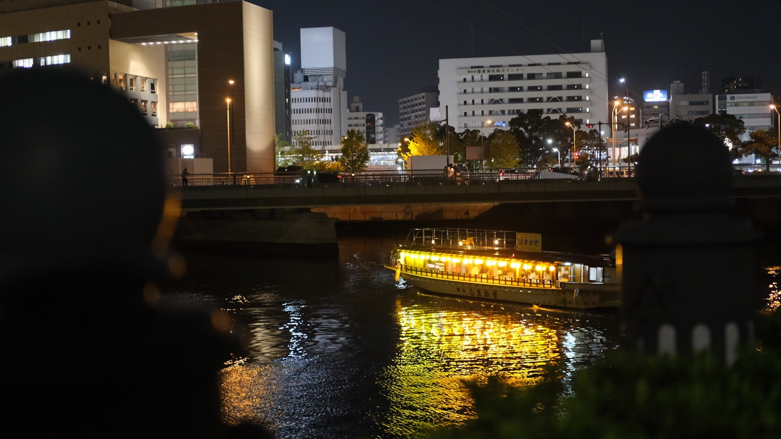 Beleuchtetes Boot, das nachts auf einem Fluss mit Stadtsilhouette treibt