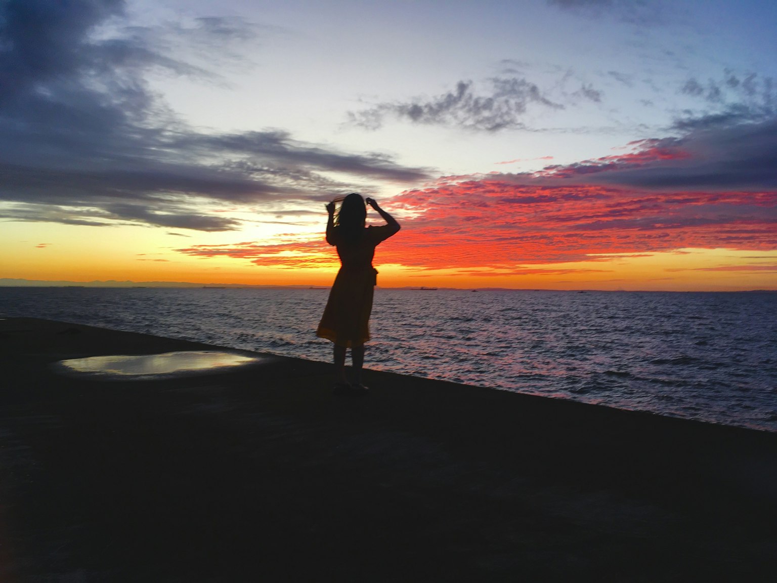 Silhouette của một người phụ nữ đứng bên bờ biển lúc hoàng hôn