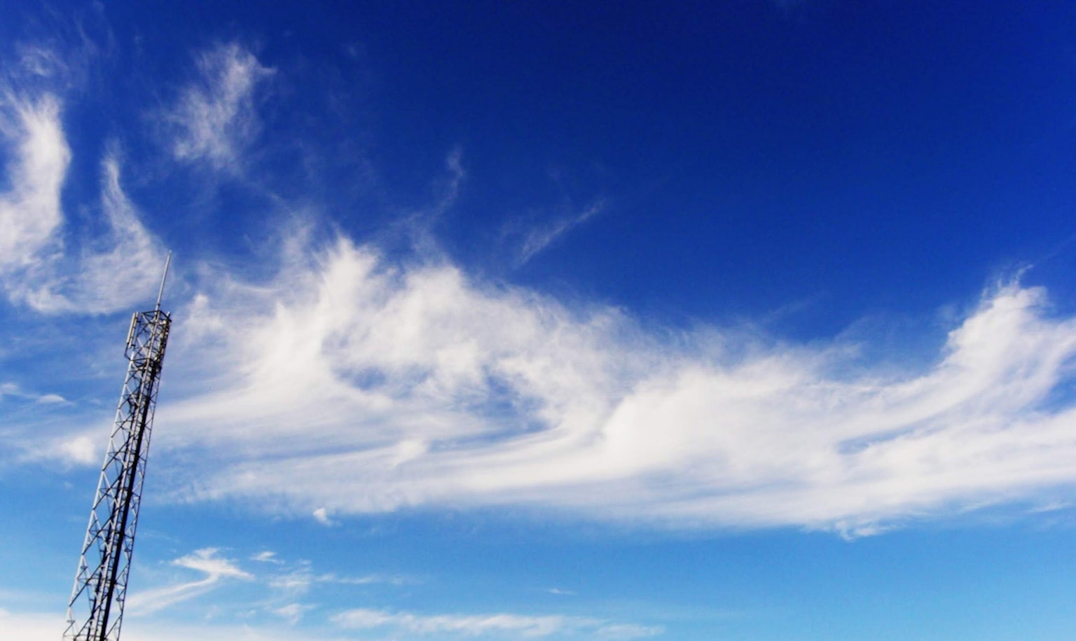 Nubes en un cielo azul con una torre de comunicación