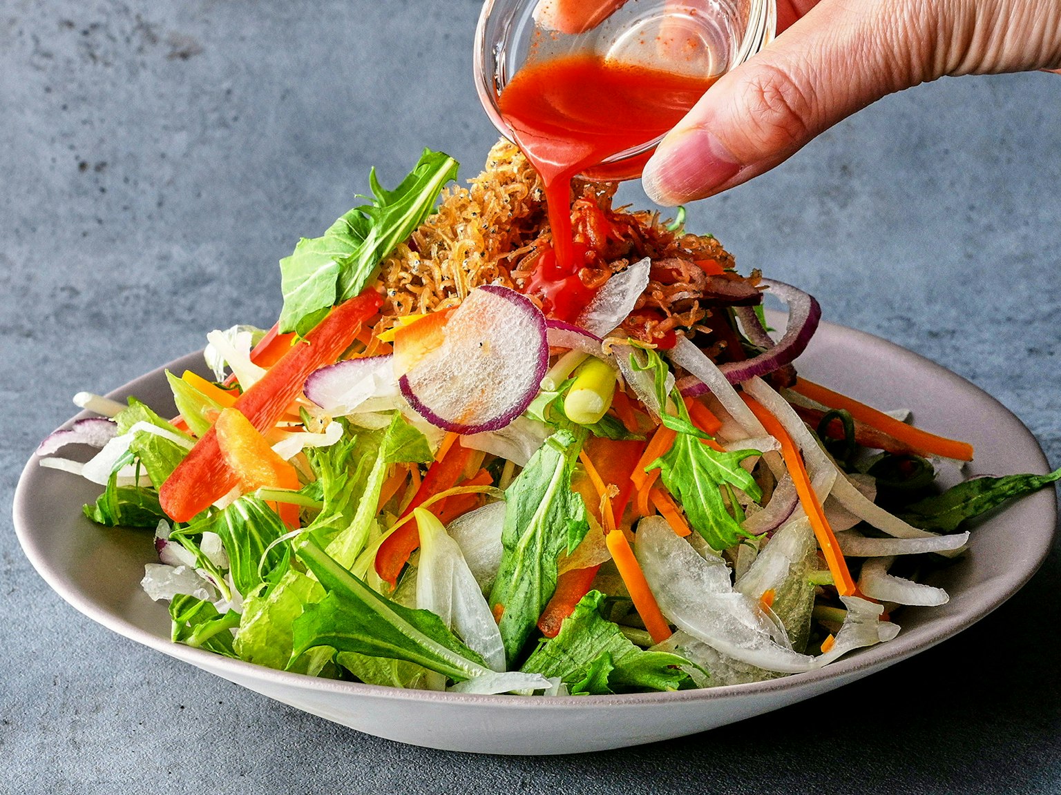 Tangan menuangkan saus di atas salad sayuran segar