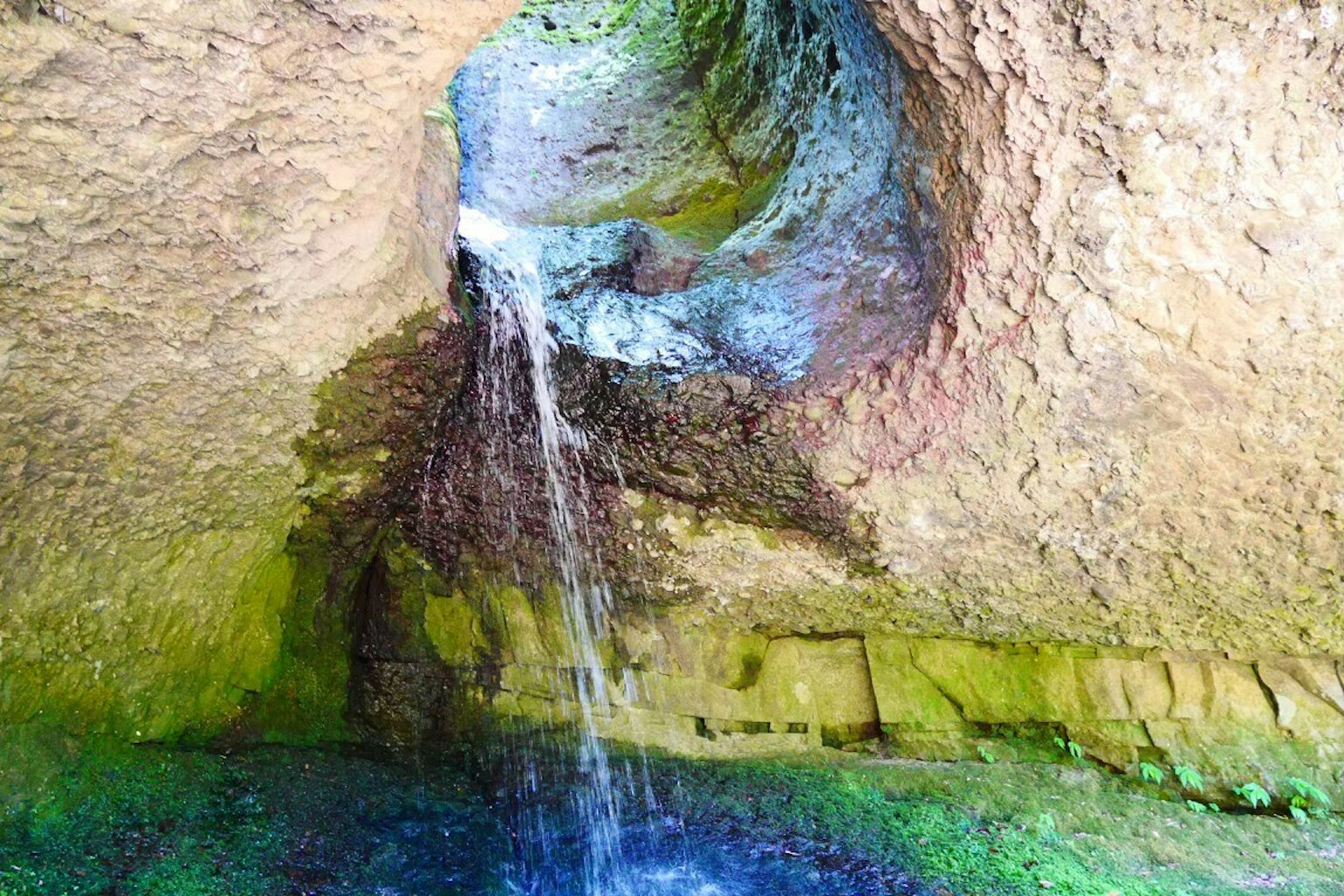 自然景观，水从洞穴流出，绿色池塘
