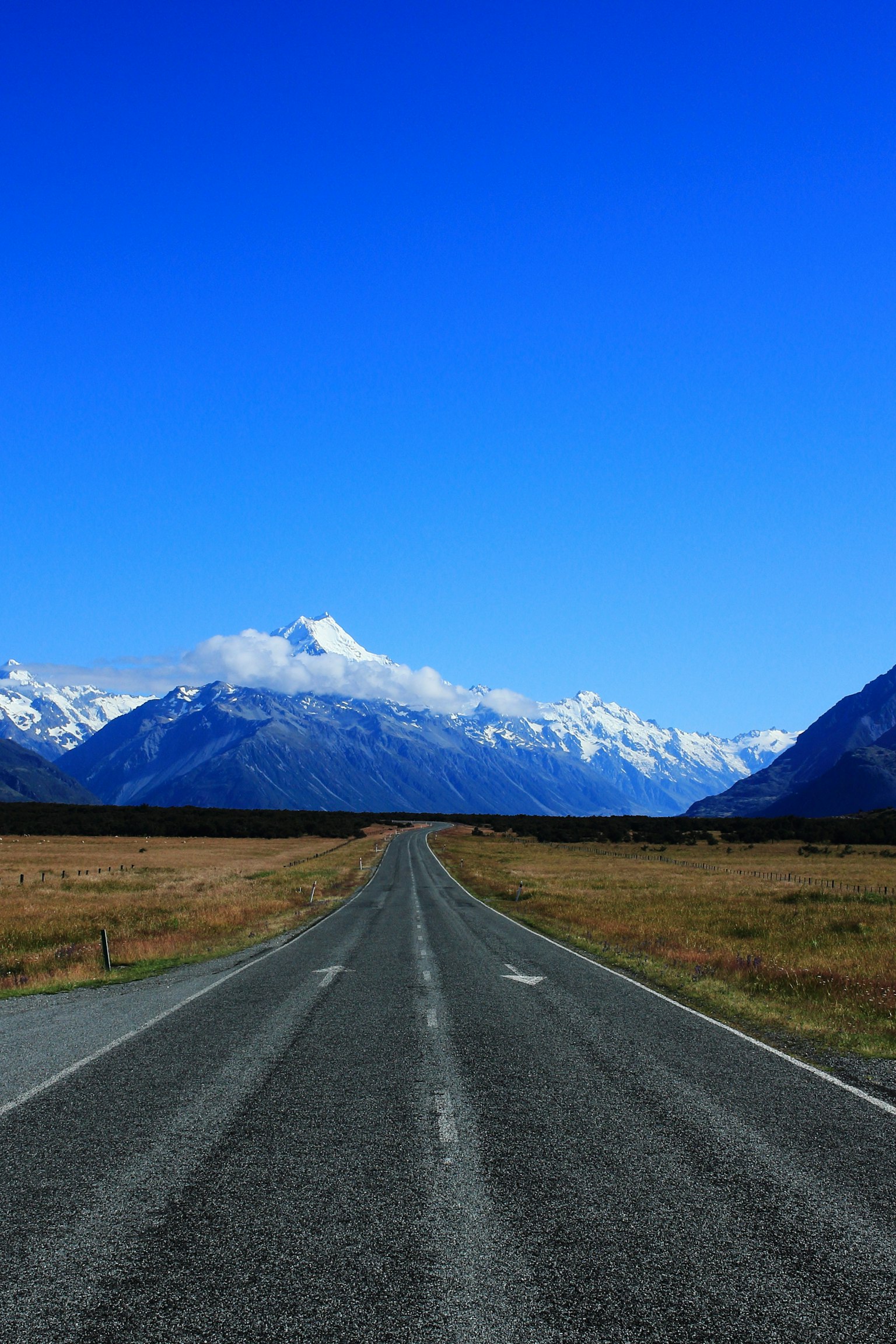 Une route s'étendant vers des montagnes enneigées sous un ciel bleu clair