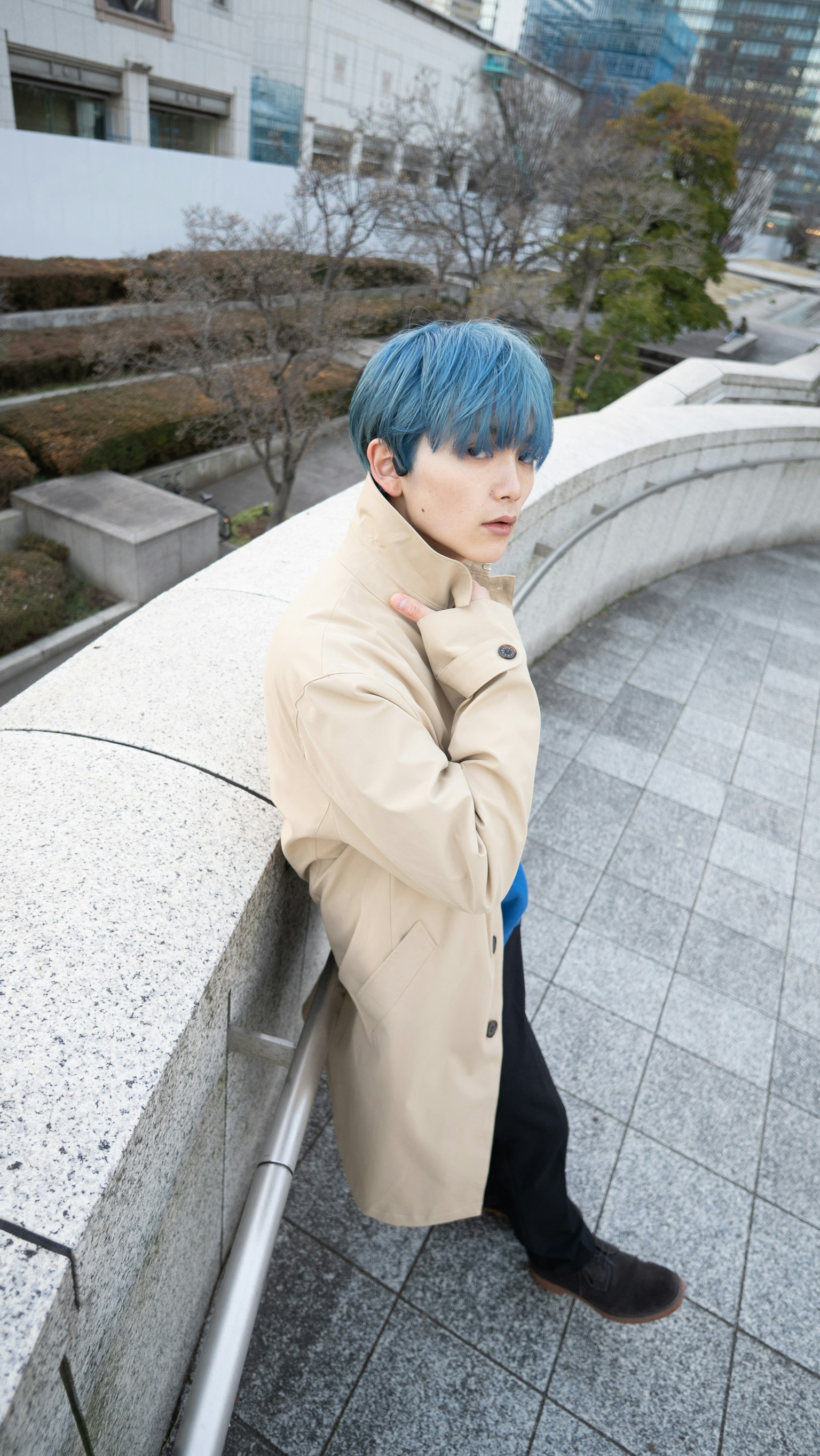 คนหนุ่มสาวที่มีผมสีน้ำเงินสวมเสื้อโค้ทสีเบจในสภาพแวดล้อมกลางแจ้ง