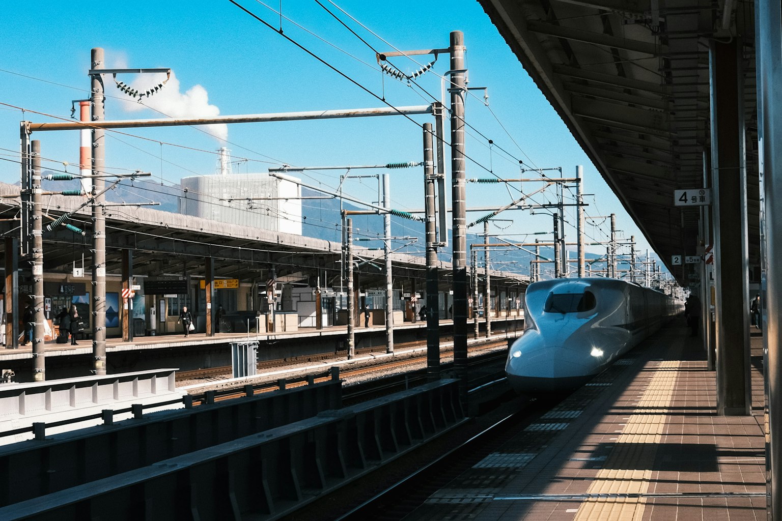 รถไฟชินคันเซ็นมาถึงสถานีกับท้องฟ้าสีฟ้าและภูเขาเป็นฉากหลัง