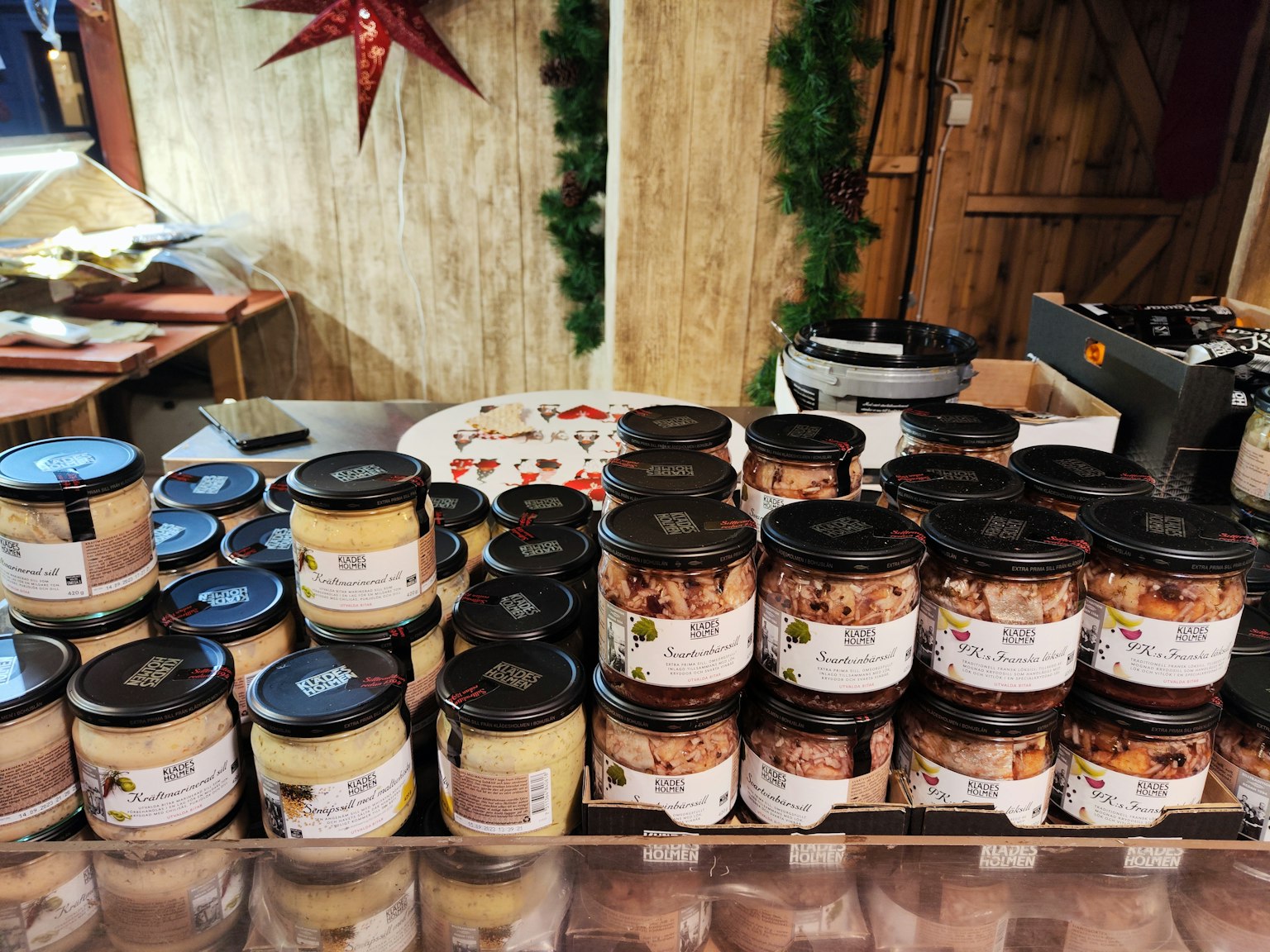 Verschiedene Gläser mit eingelegten Produkten auf einem Tisch auf einem Weihnachtsmarkt mit dekorativem Hintergrund