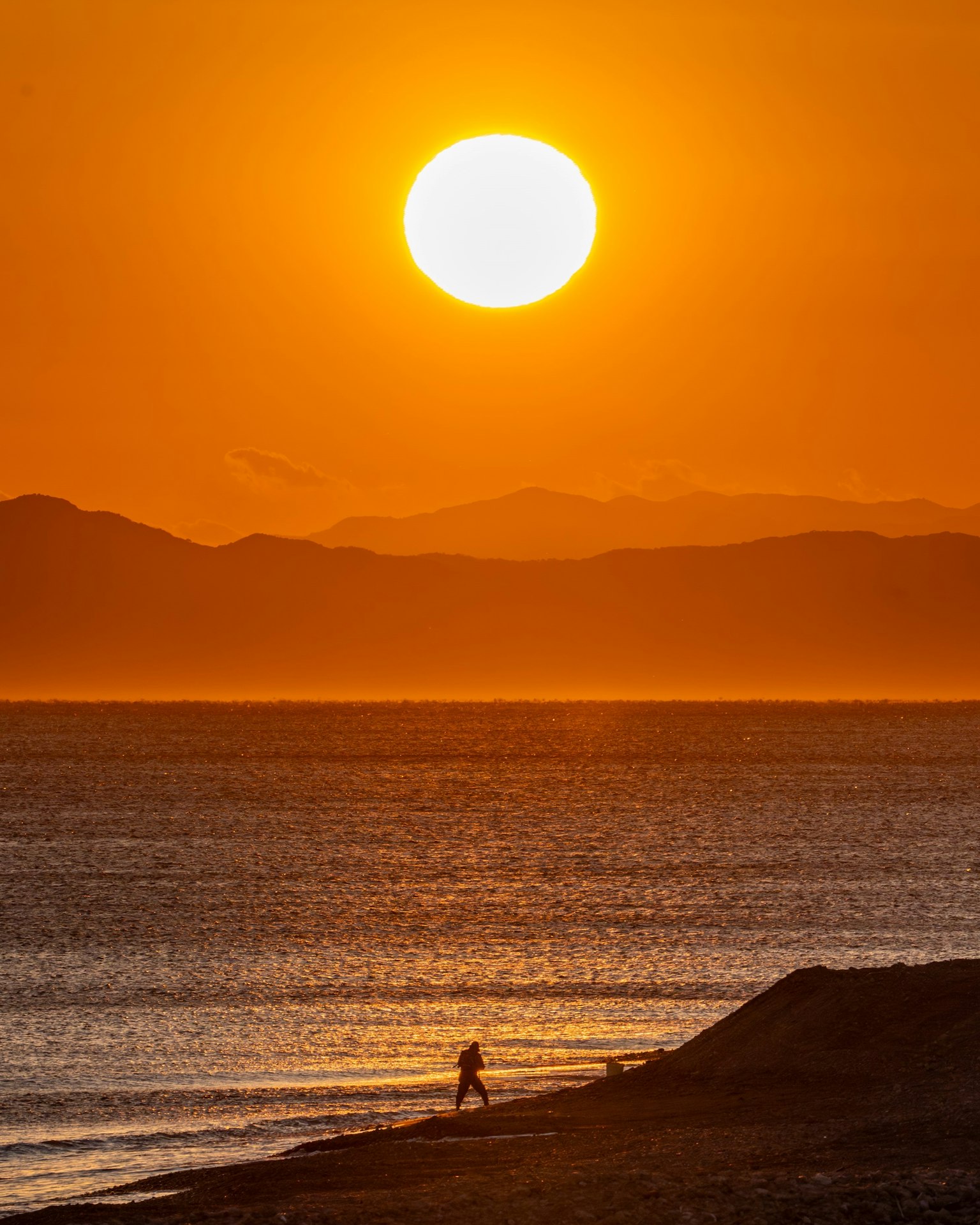 Silhouette di una persona che cammina lungo la spiaggia al tramonto
