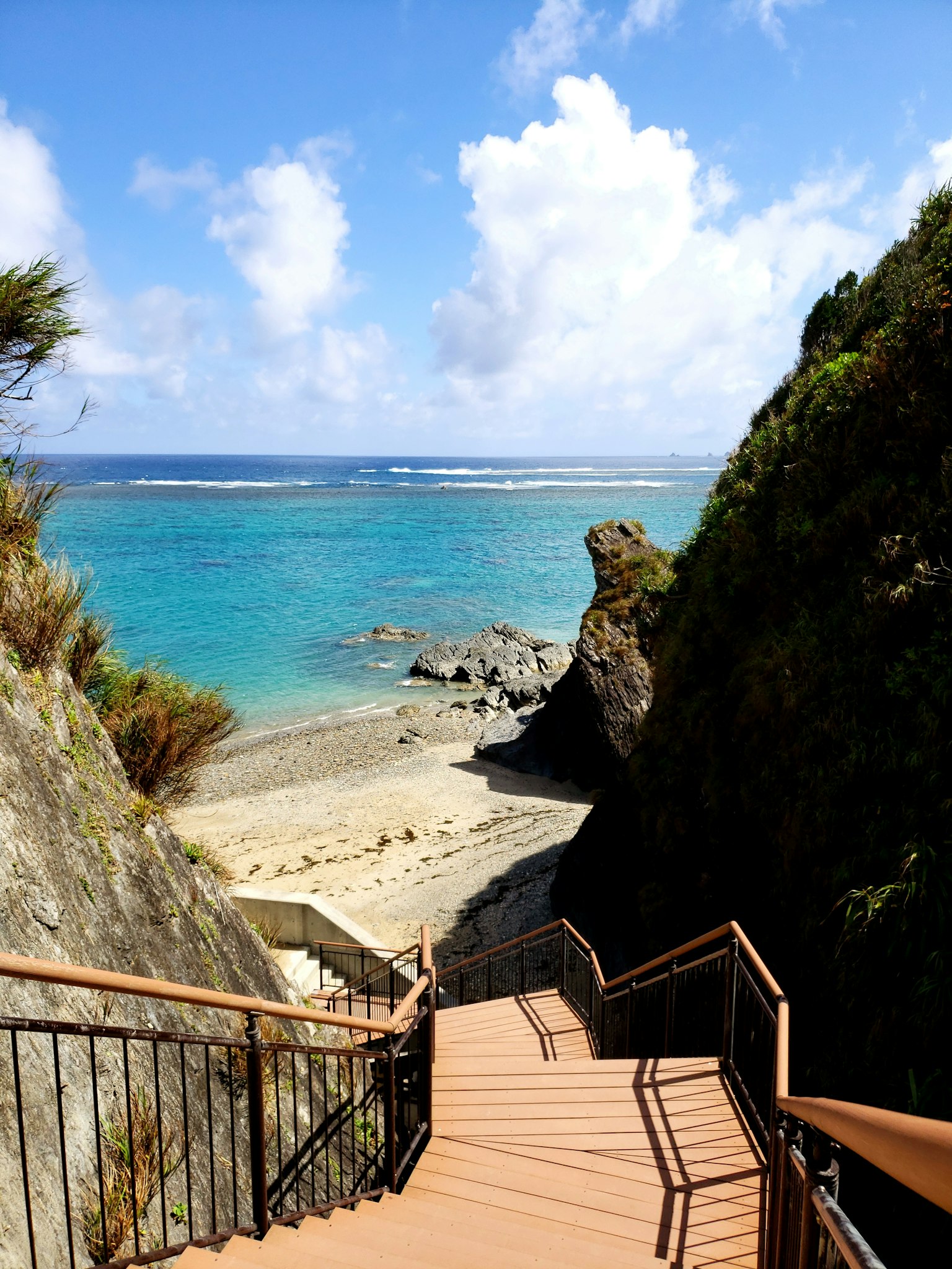 海滩的风景，碧绿的海水和白色的云朵，通往下方的楼梯