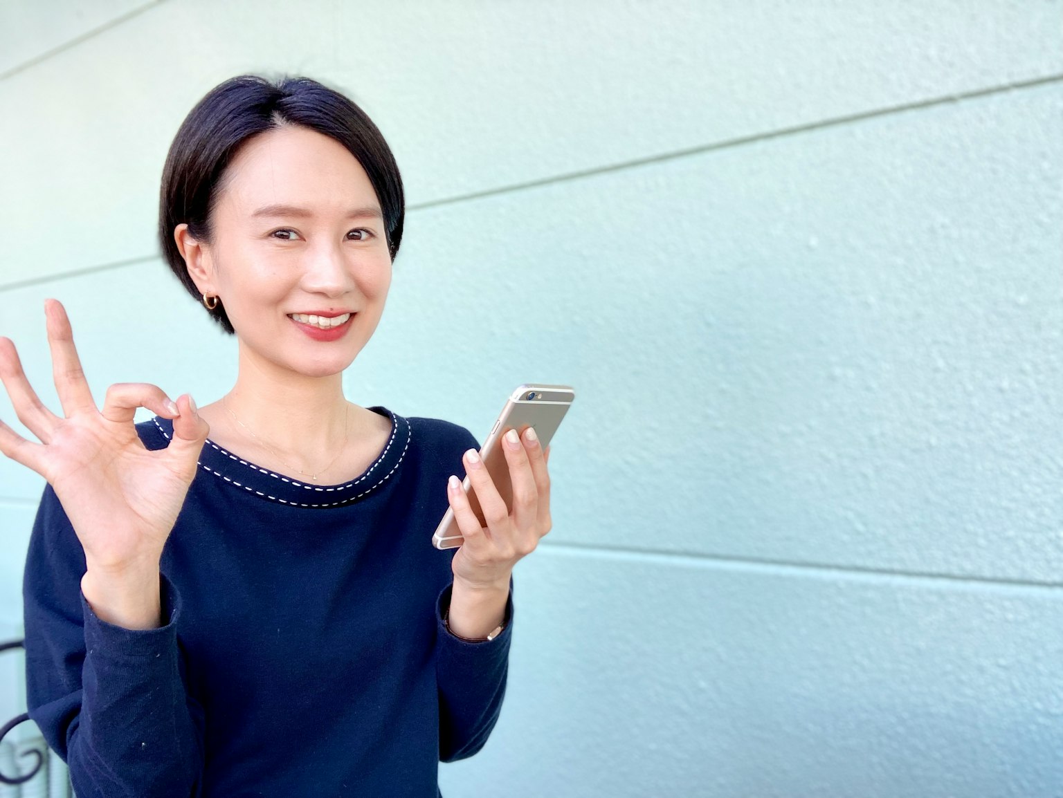 Donna sorridente che fa il segno OK mentre tiene uno smartphone