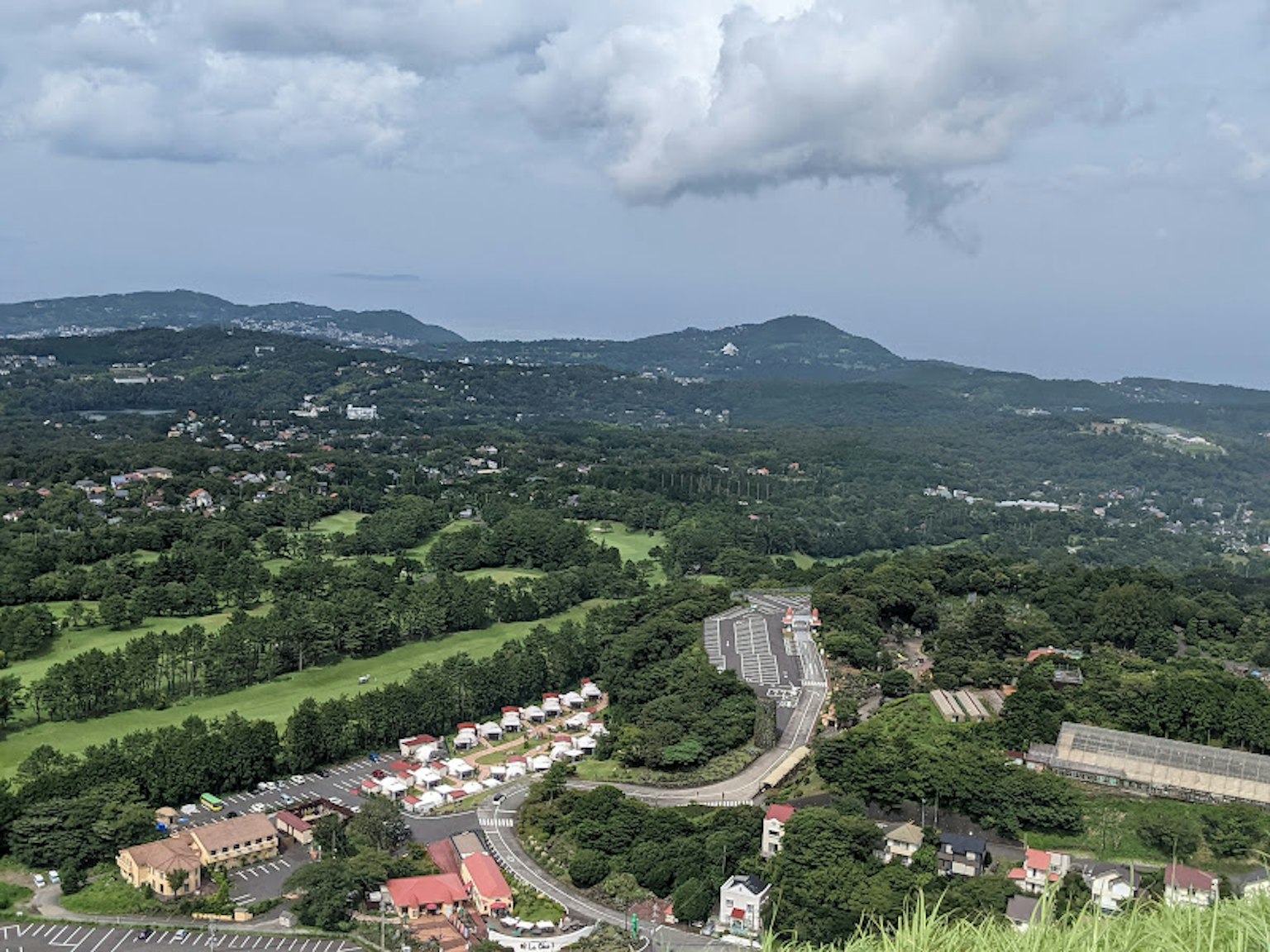 ภาพทิวทัศน์ที่มีเนินเขาสีเขียวและวิวทะเลพร้อมถนนที่มีบ้านเรียงราย