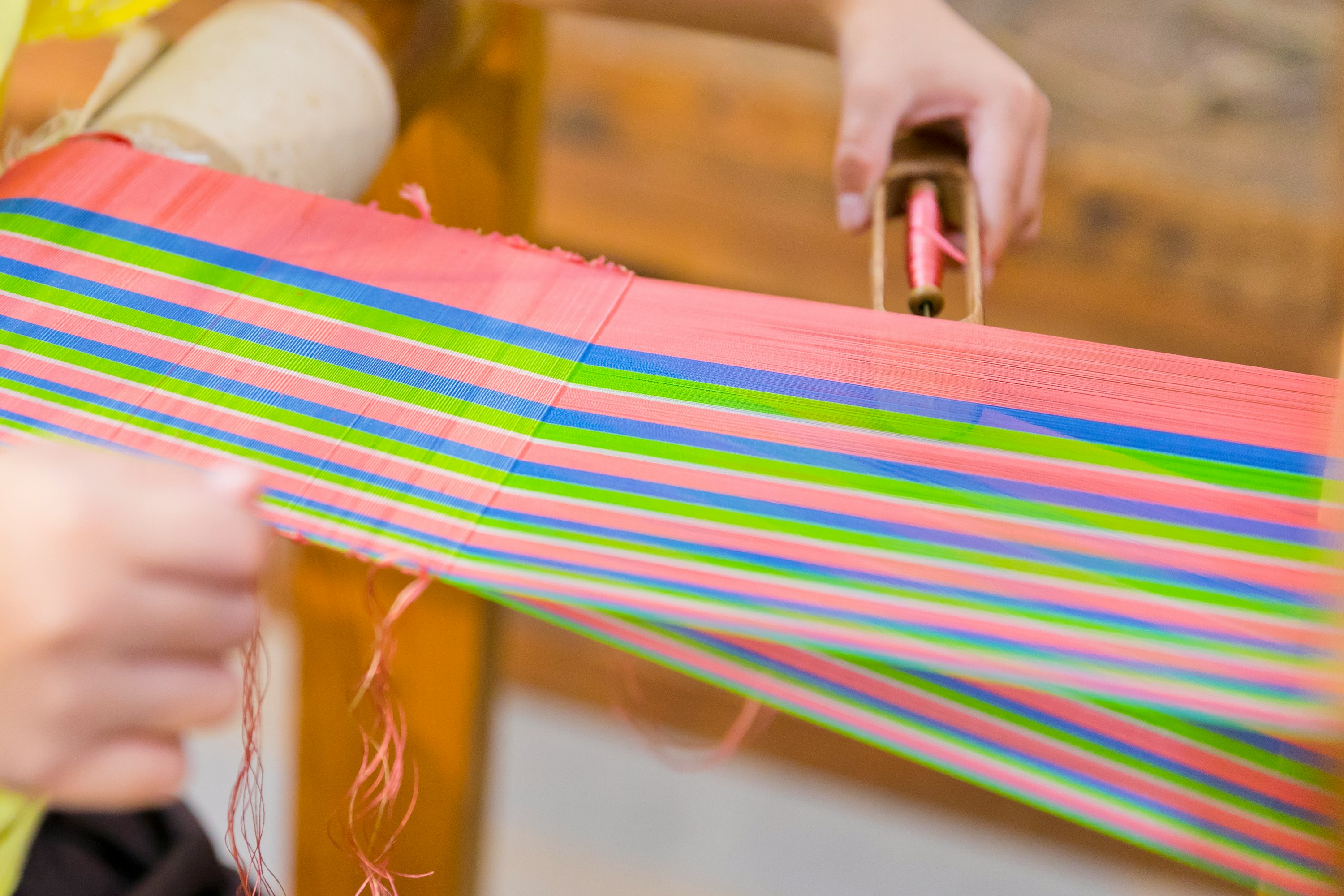 hands weaving a colorful striped fabric