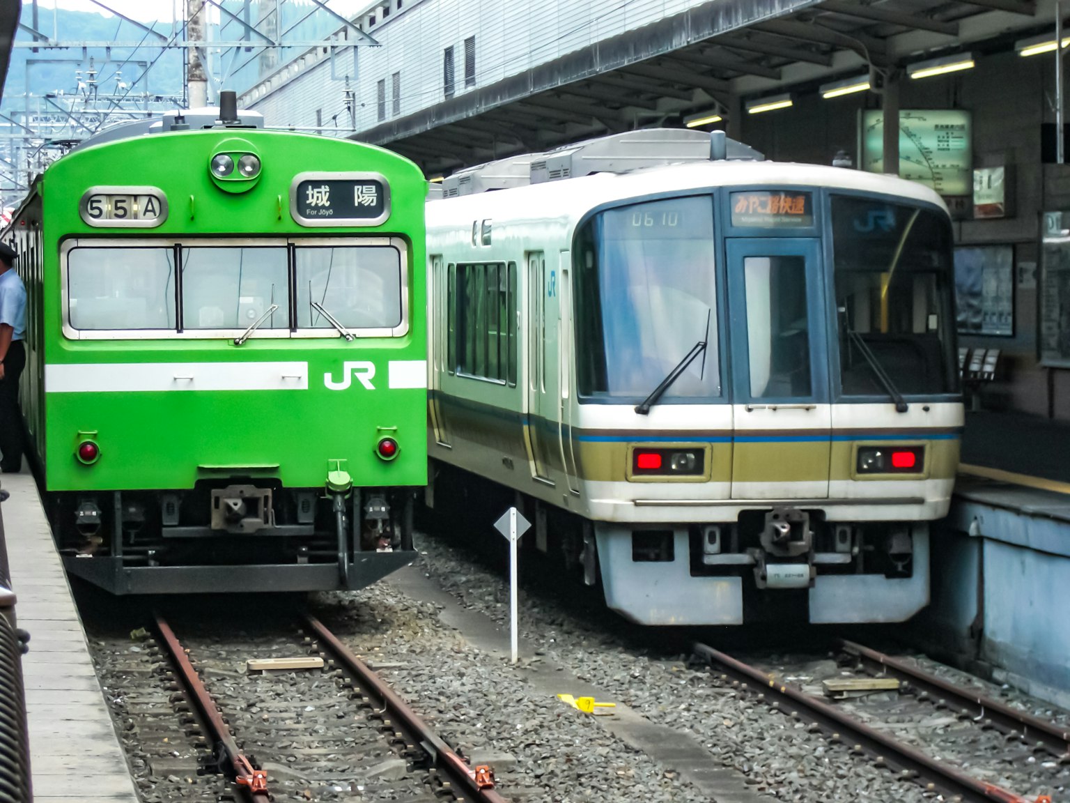 一列綠色的JR火車和一列白色的特快列車並排停靠在車站