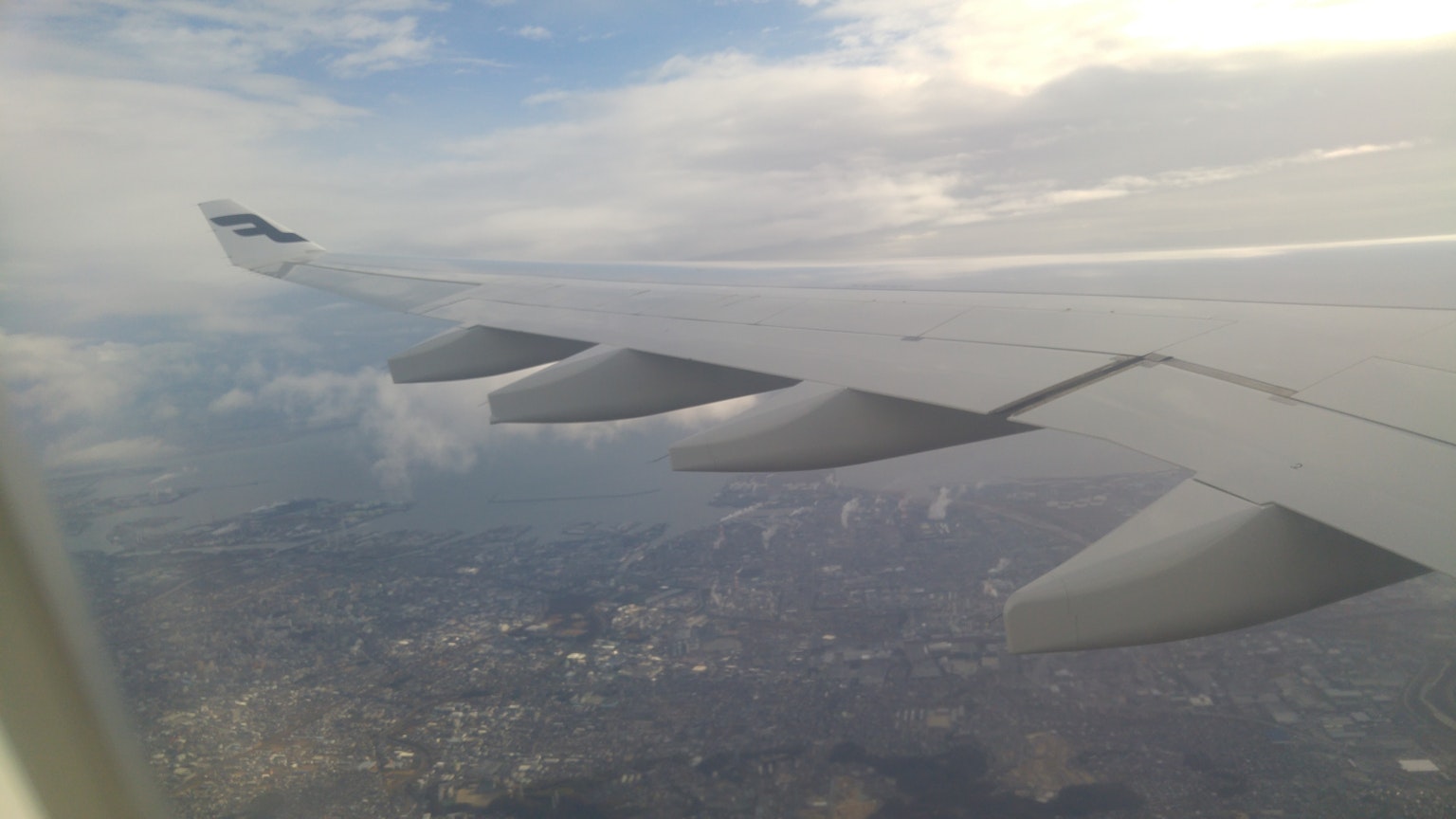 View of airplane wing against a backdrop of clouds and land below
