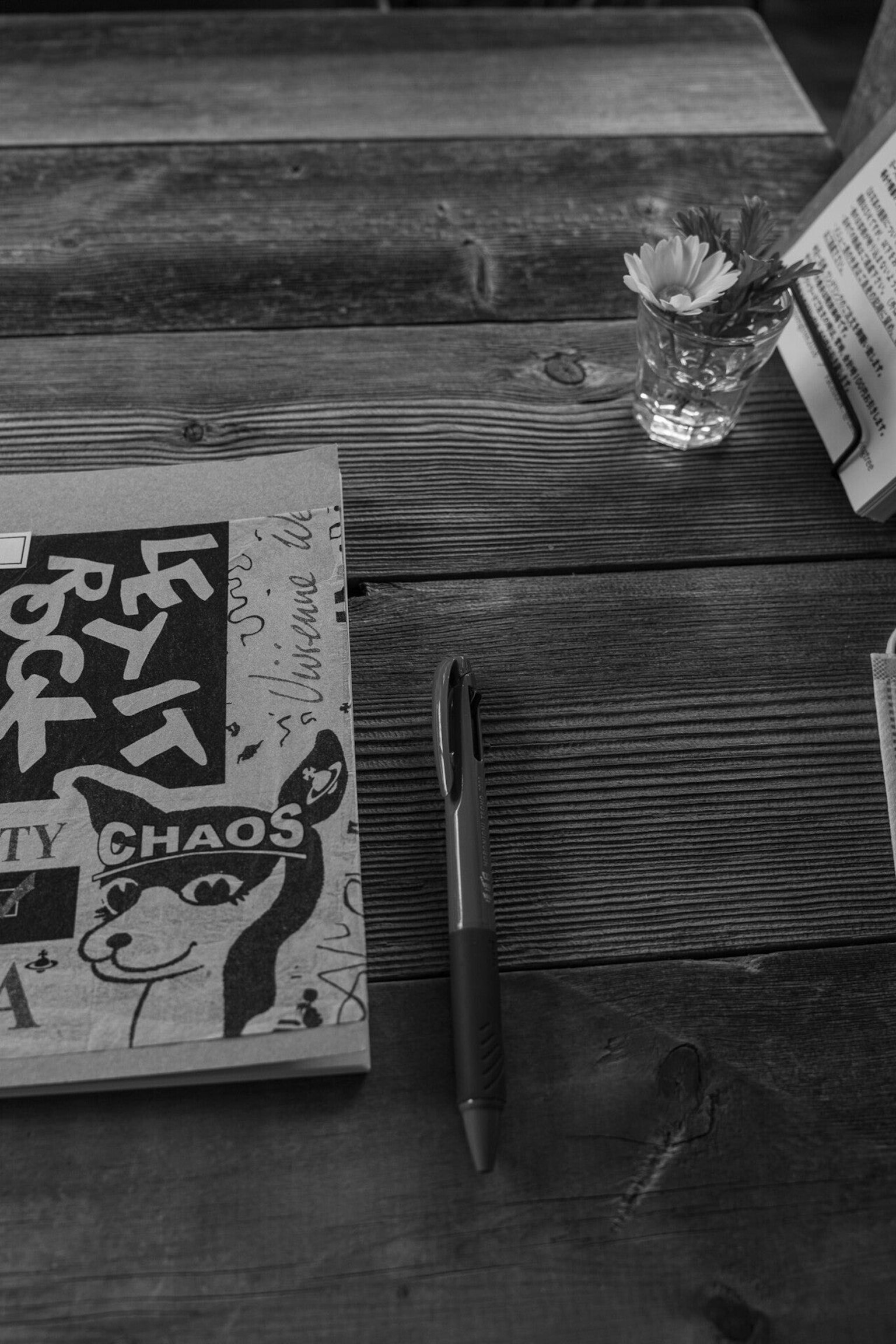 Magazine with chaotic design and pen on a wooden table small vase with flowers nearby