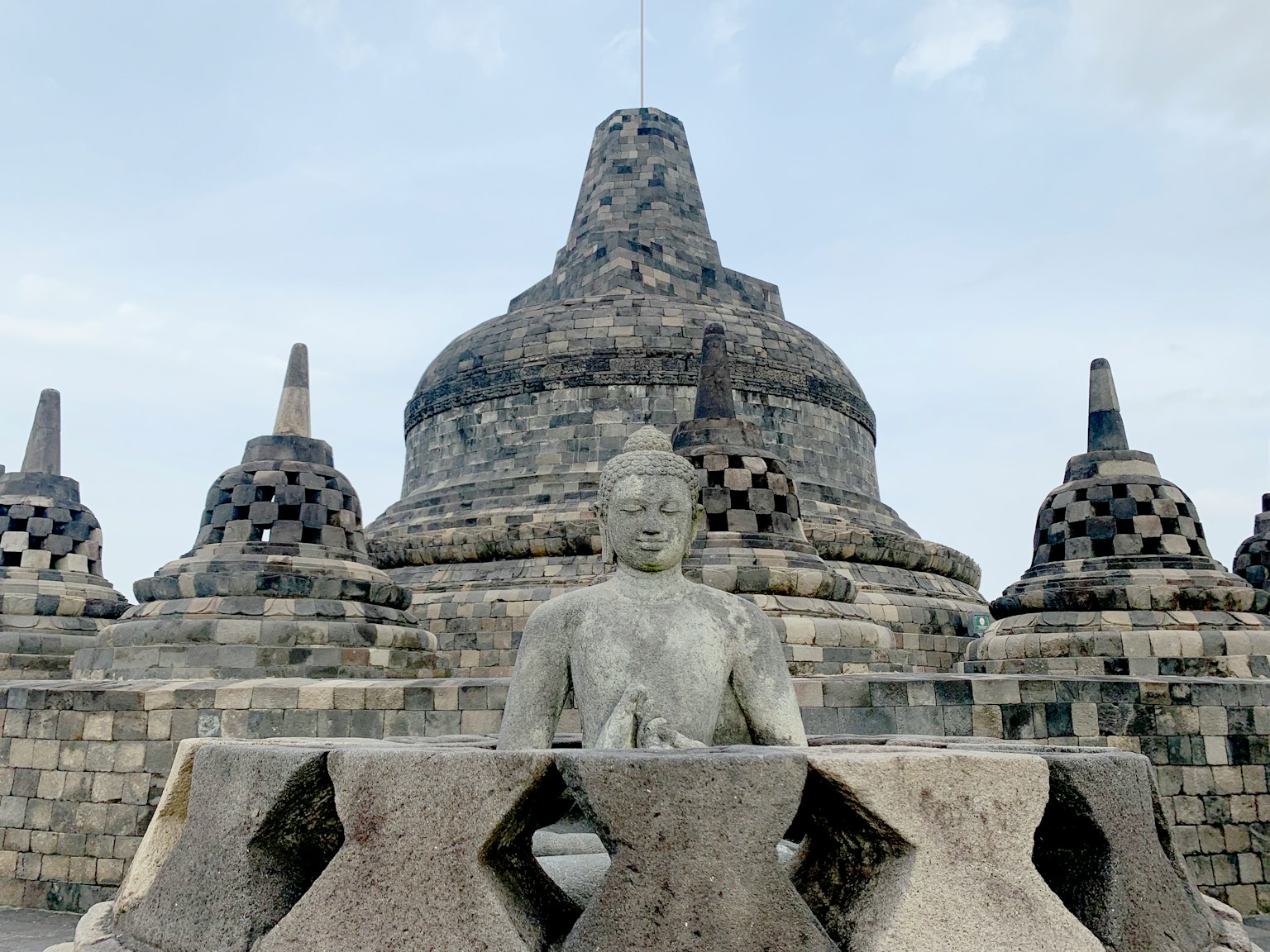 Buddha statue in front of Borobudur temple with stupas in the background