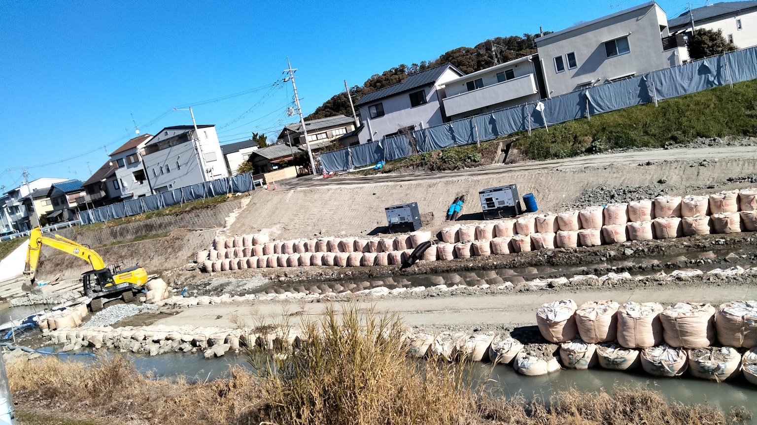 Cantiere di costruzione lungo un fiume con camion e macchinari pesanti