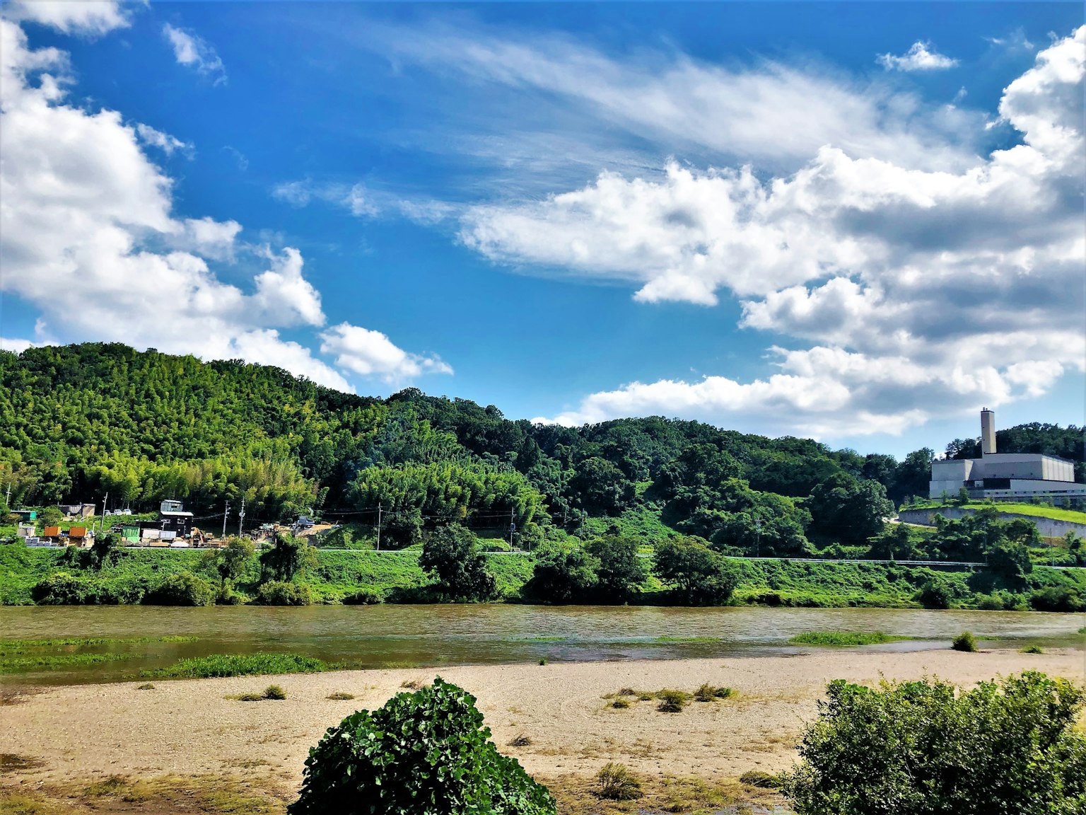 ทิวทัศน์ที่สวยงามของเนินเขาสีเขียวและแม่น้ำใต้ท้องฟ้าสีฟ้าพร้อมเมฆขาว