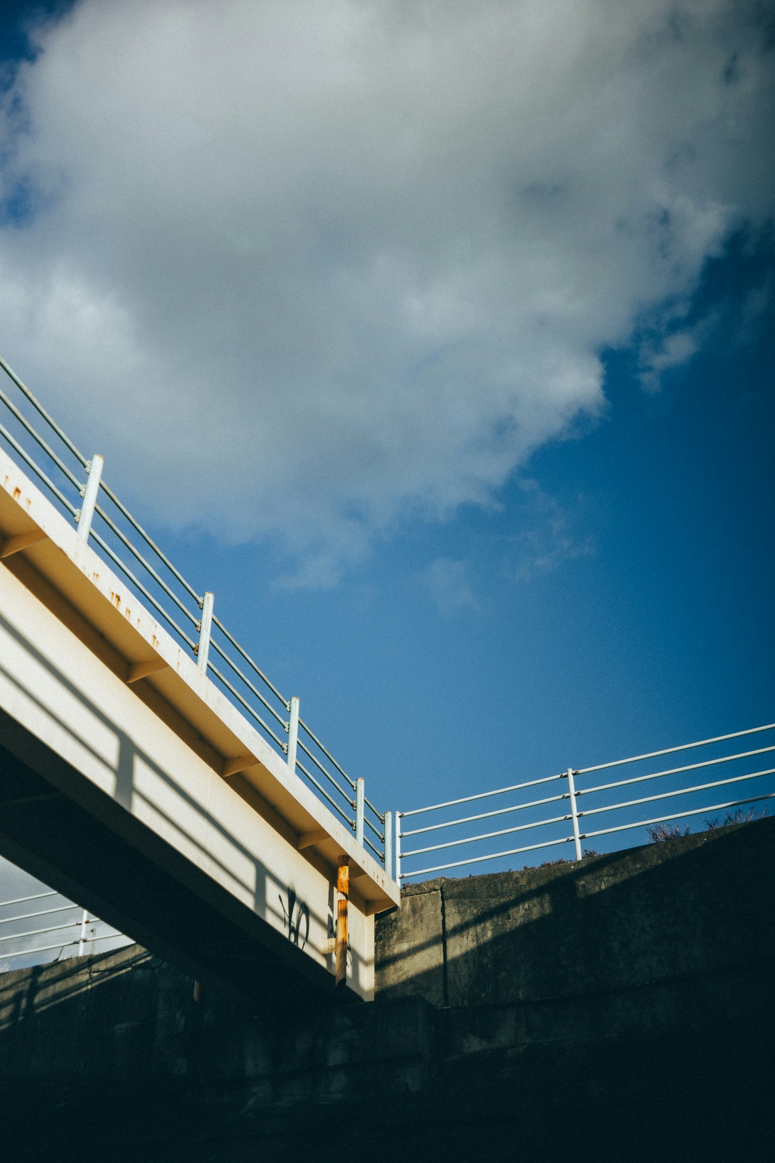 Blick auf eine Brücke von unten mit blauem Himmel und weißen Wolken