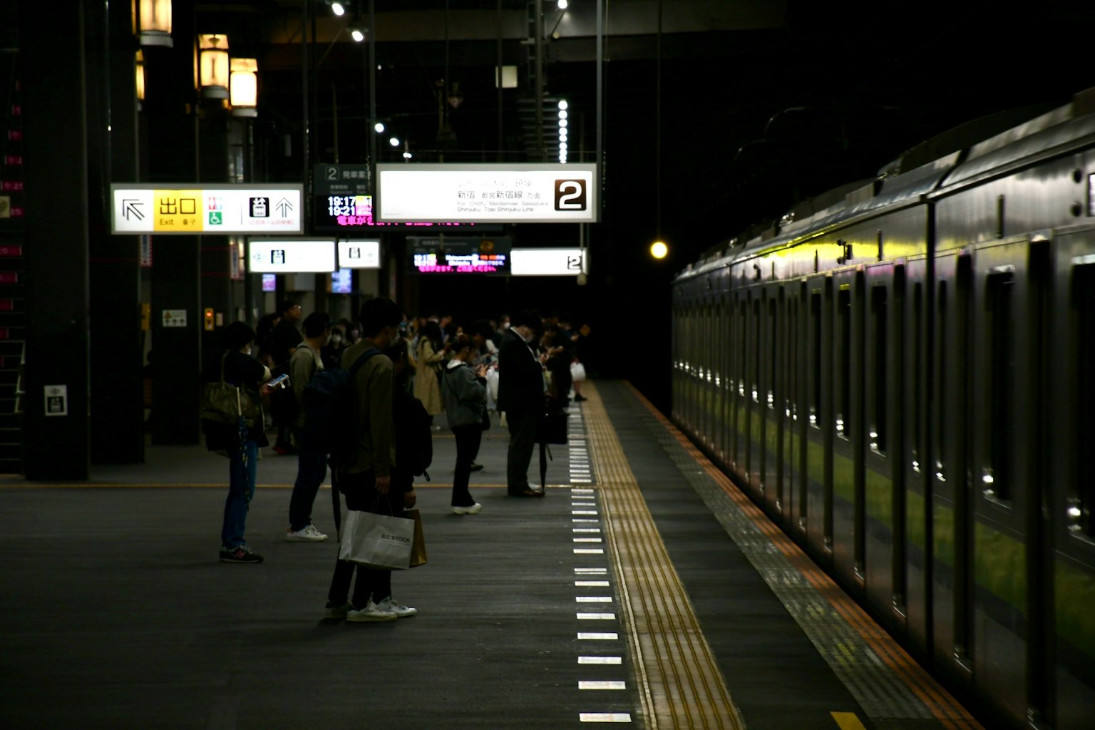 Passengers waiting for a train at a night station with bright signs
