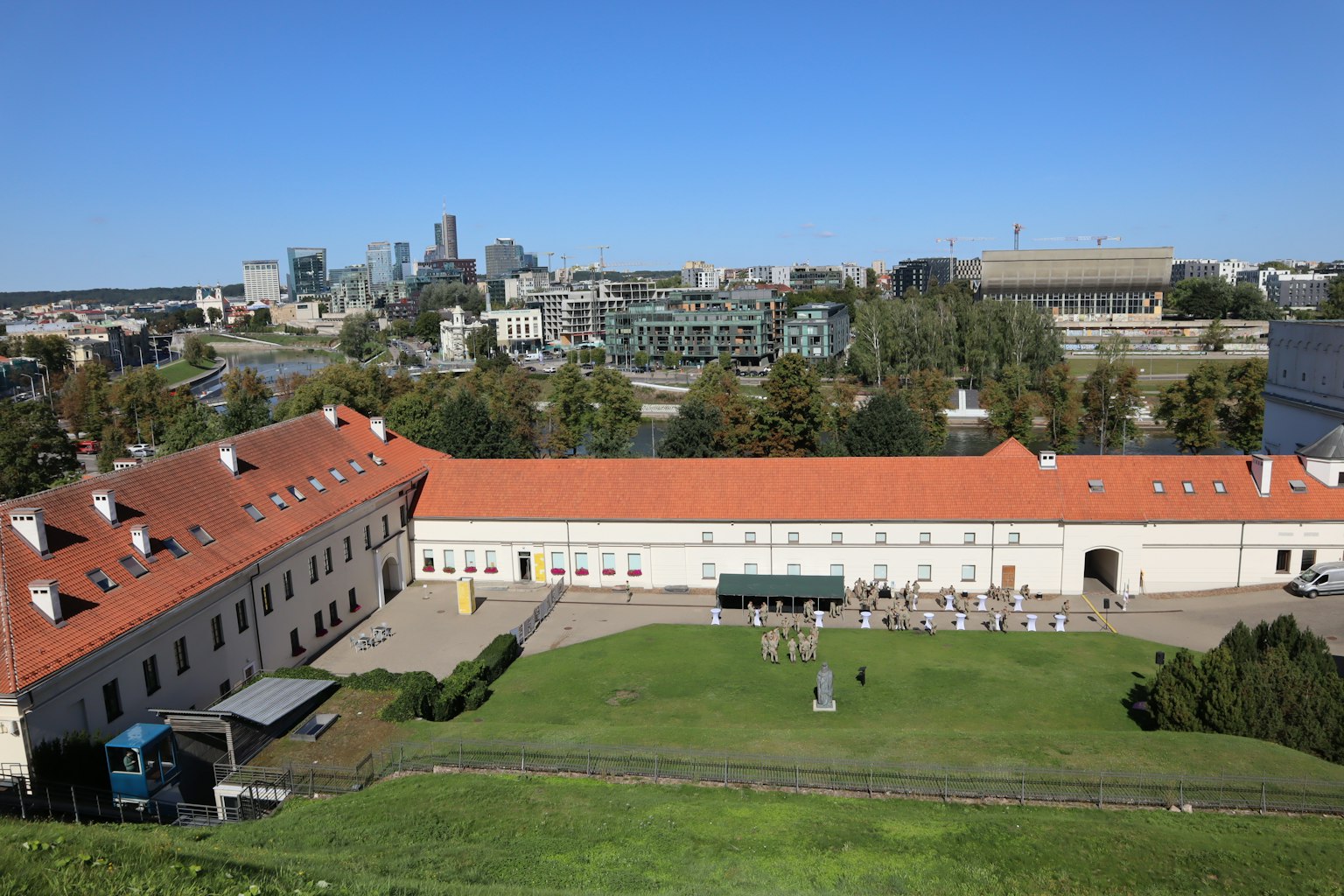Vista panorámica de un edificio con techos rojos y céspedes verdes frente a un horizonte urbano