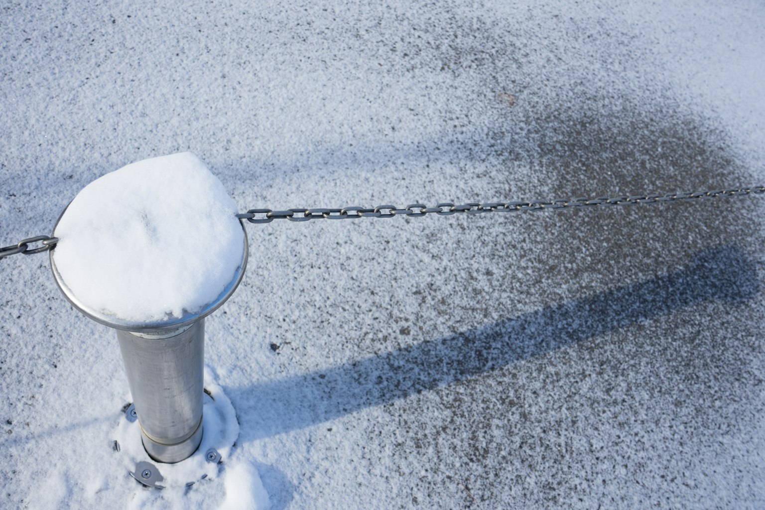 Schneebedeckter Pfosten mit Kette und Schatten