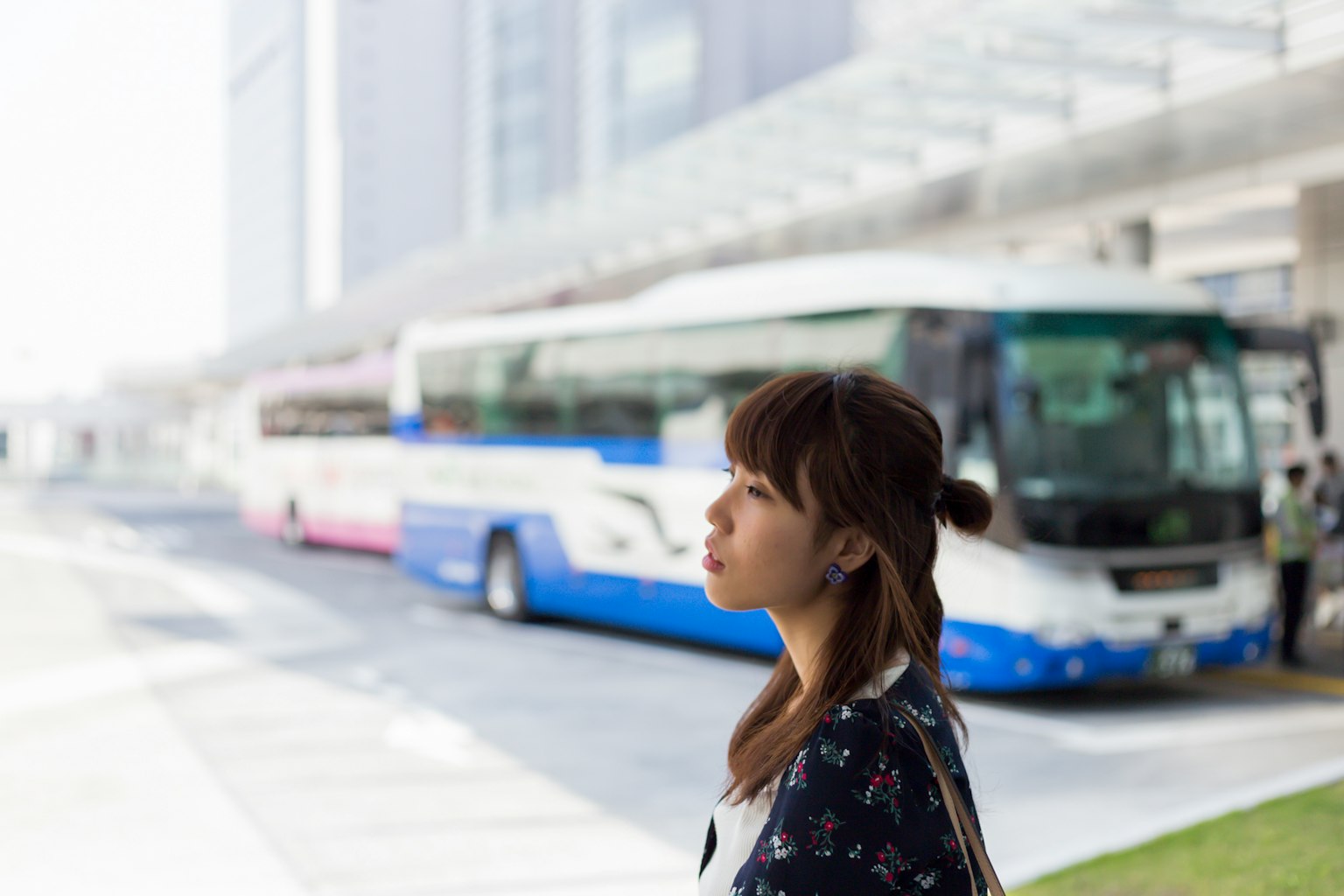 Perfil de una mujer esperando en una parada de autobús con autobuses al fondo