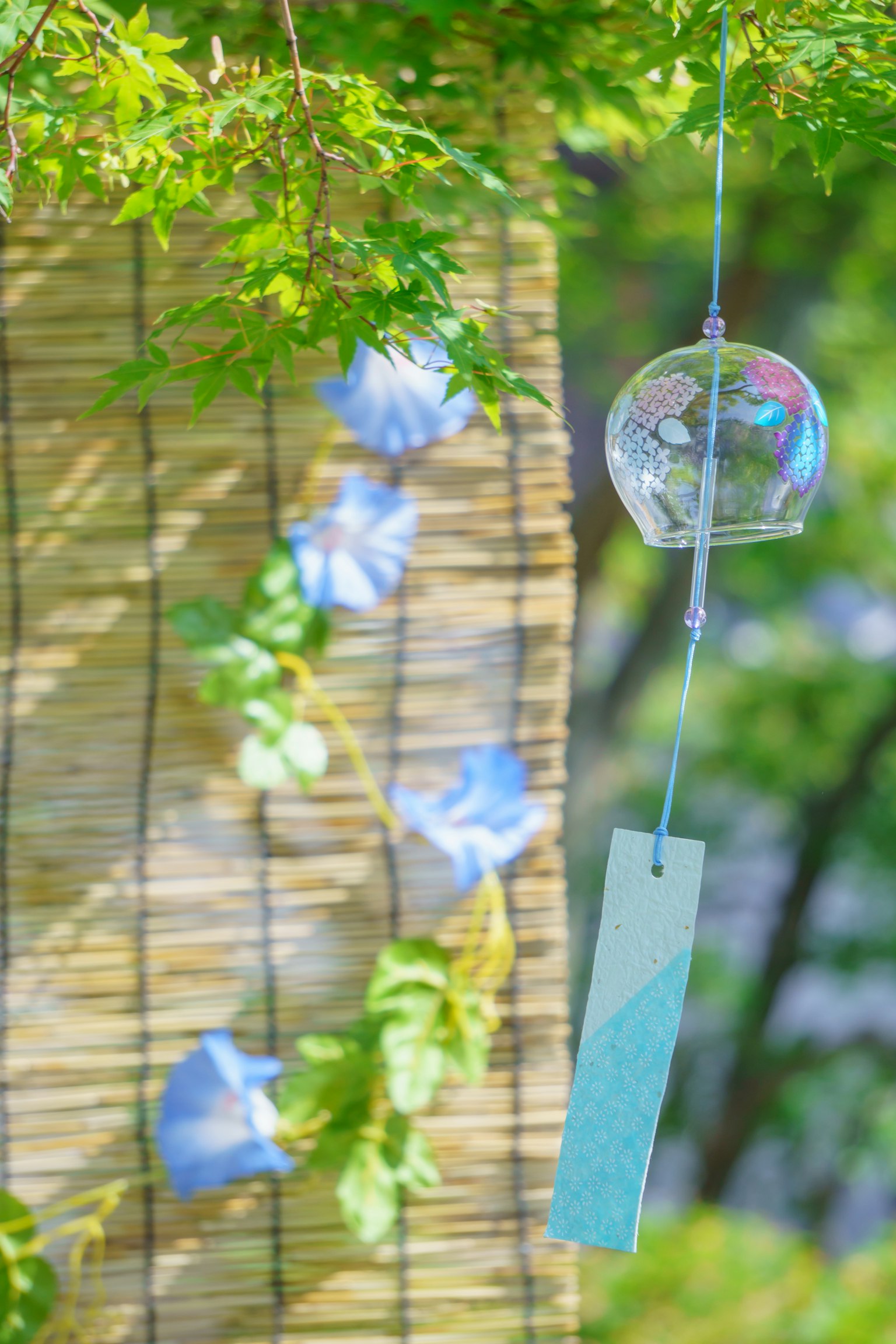 Une cloche à vent suspendue parmi des feuilles vertes avec des fleurs de gloire du matin en arrière-plan