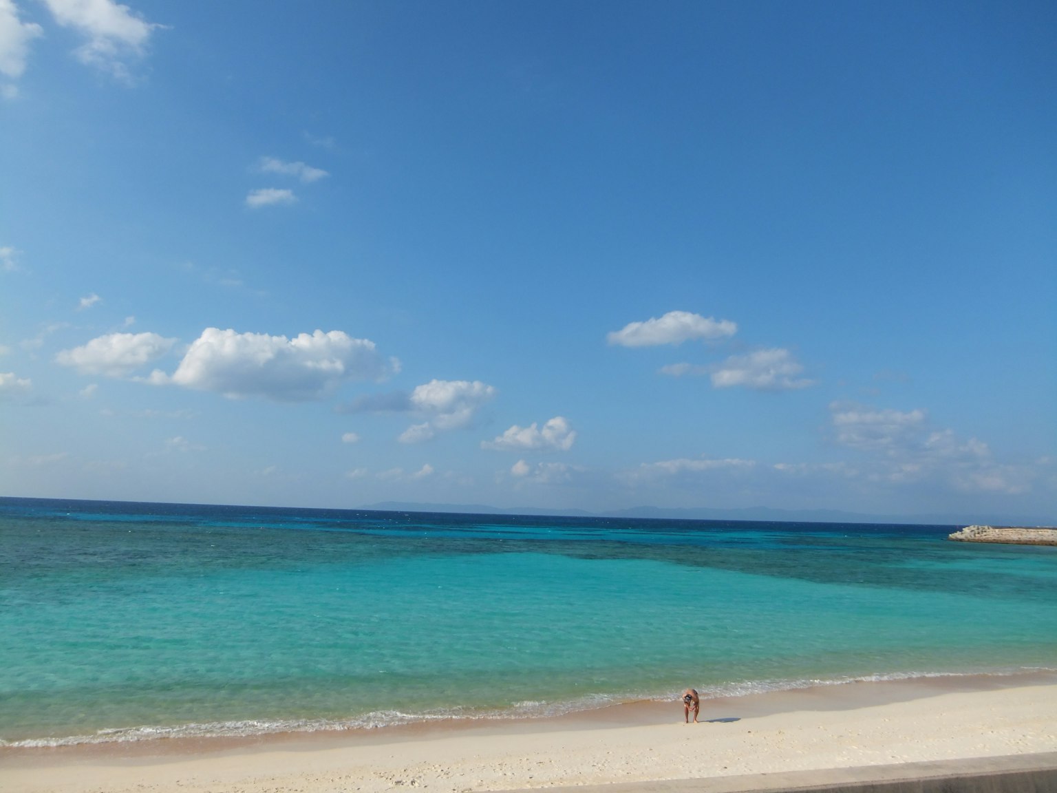 Spiaggia panoramica con oceano blu e sabbia bianca con una figura solitaria