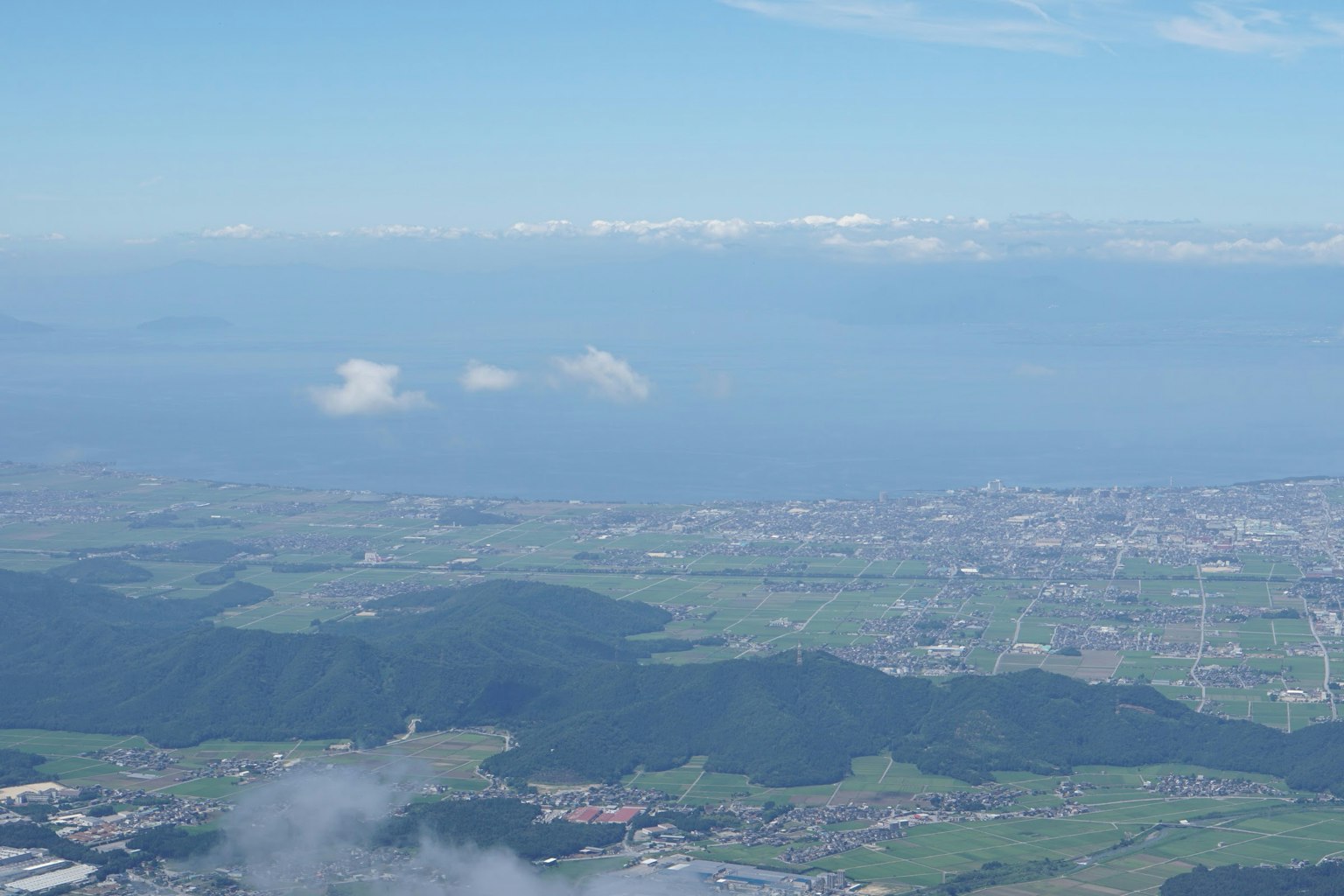 Vista aérea que muestra un océano azul y nubes con tierras verdes y áreas urbanas