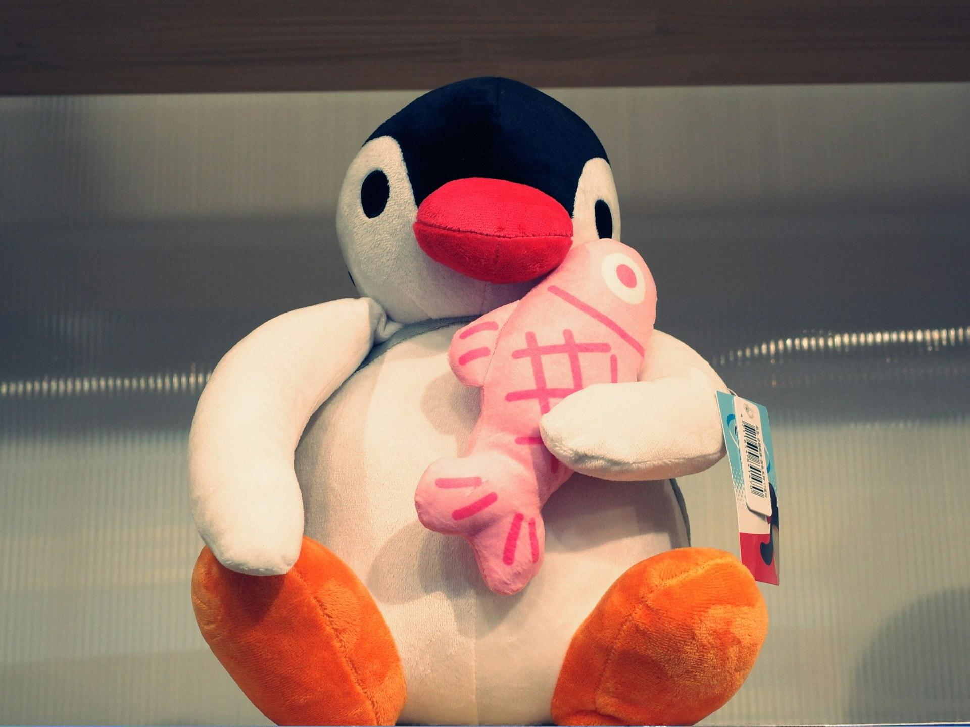 かわいいペンギンのぬいぐるみがピンクの魚を抱えている