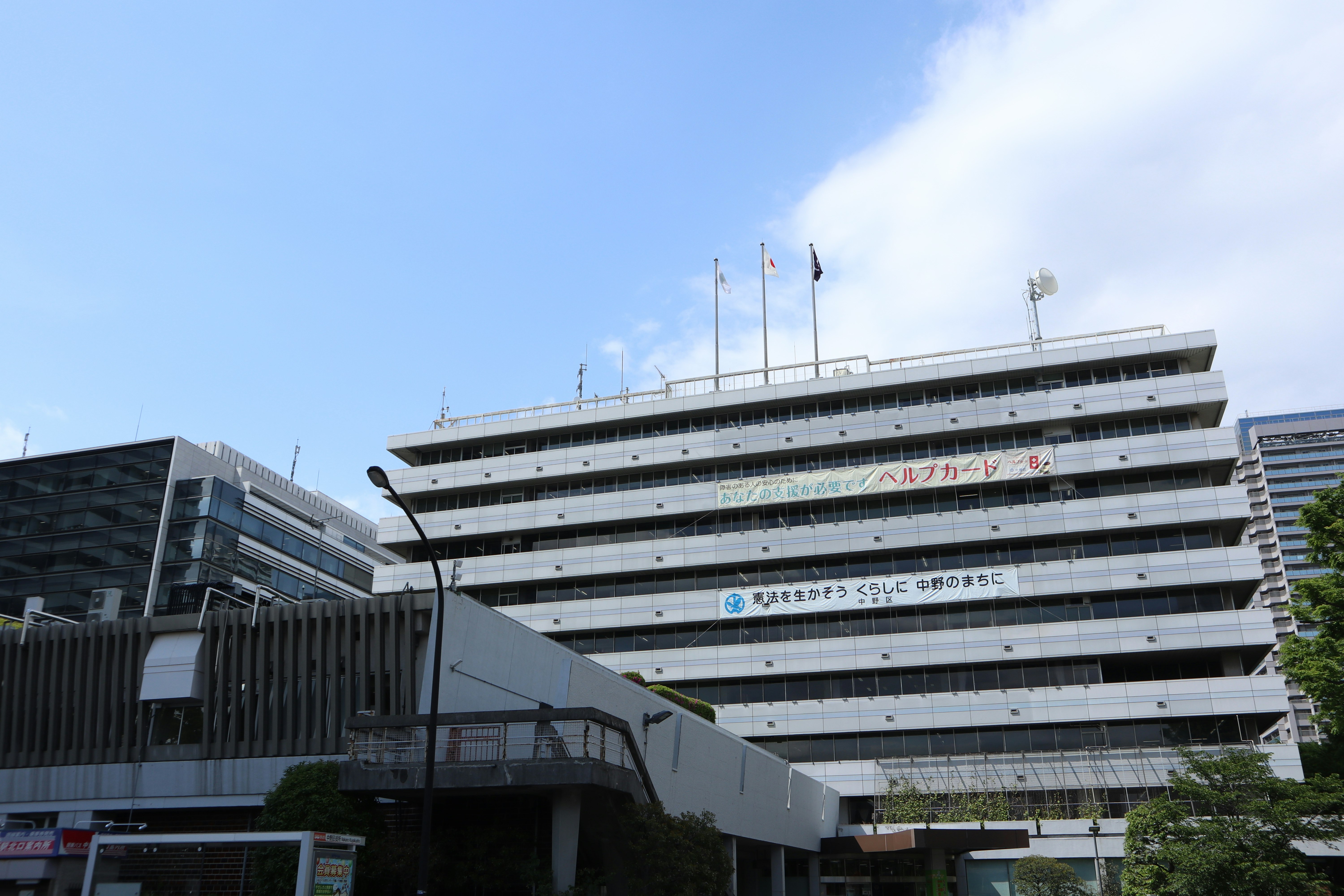 白い高層ビルと屋上の国旗が並ぶ建物外観
