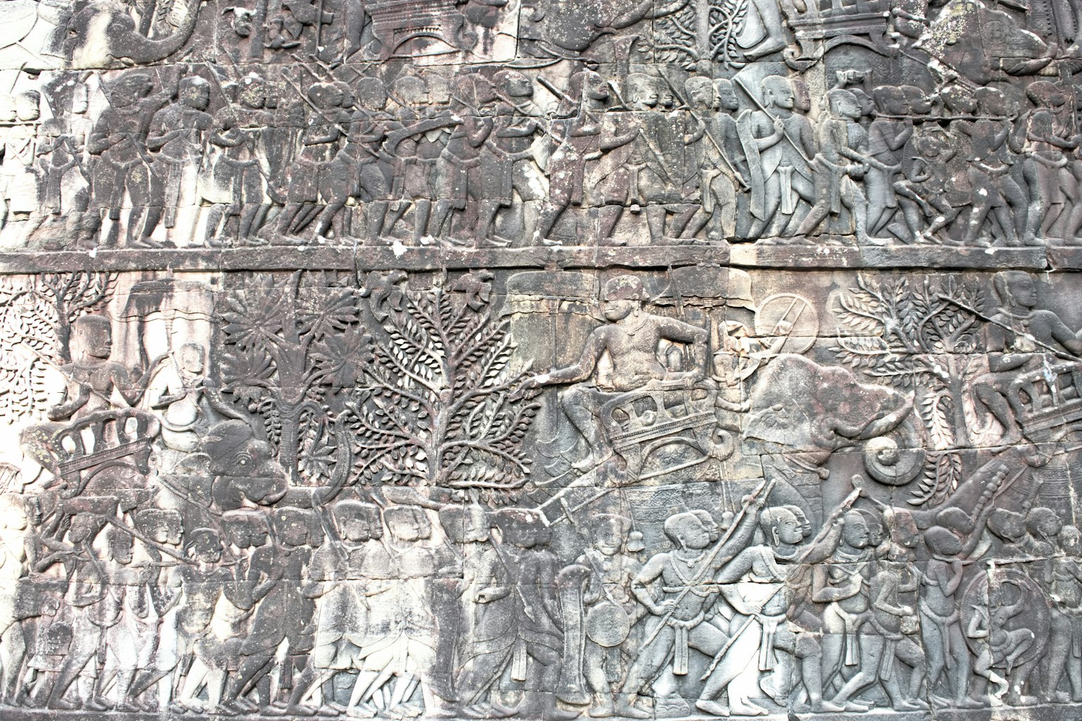 Detailed carved section of an ancient stone wall depicting warriors and animals