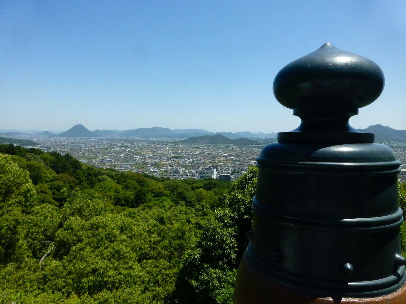 Black decorative structure with lush green mountains and city view in the background