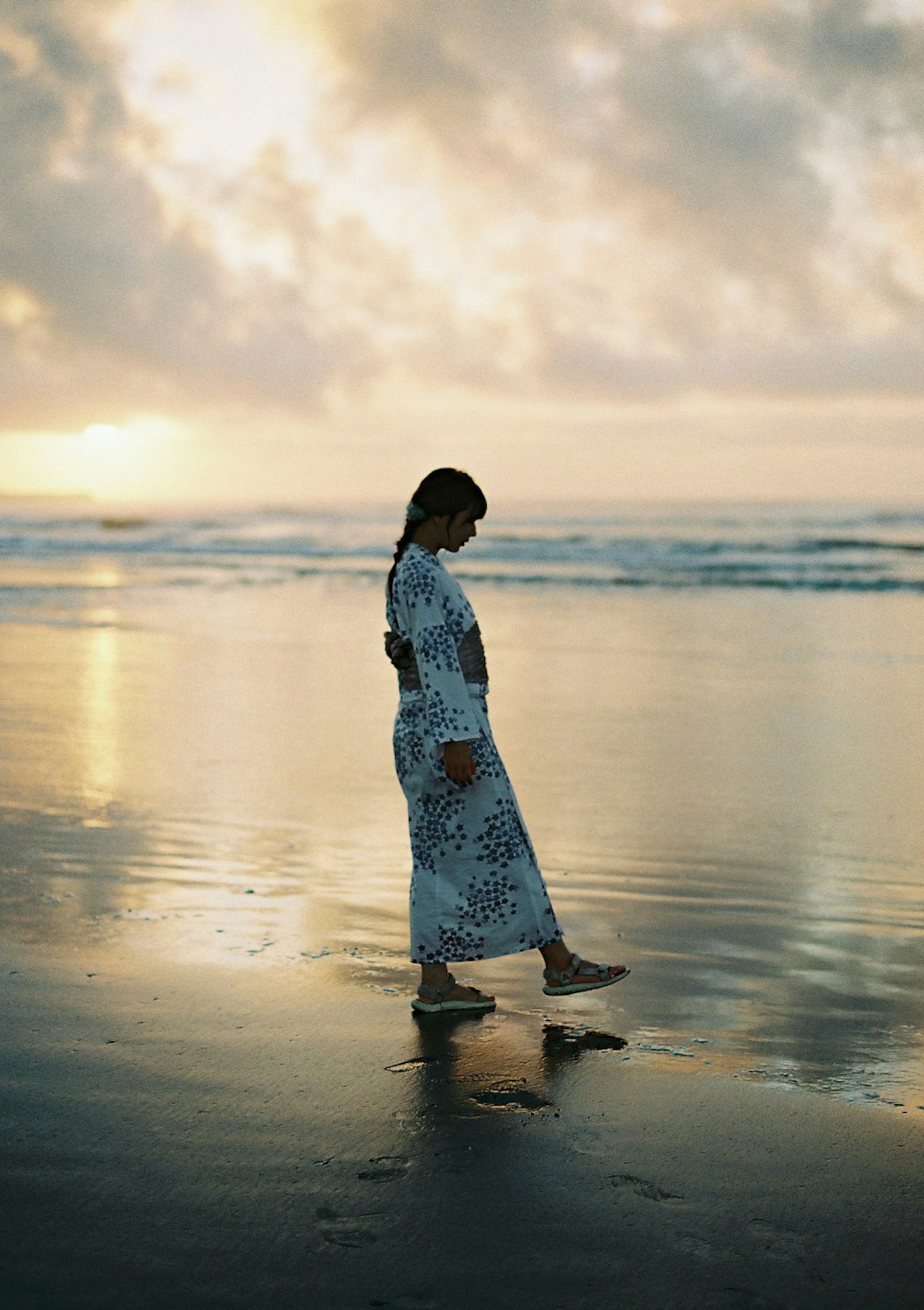 Silhouette di una donna che cammina sulla spiaggia al tramonto con riflessi sull'acqua