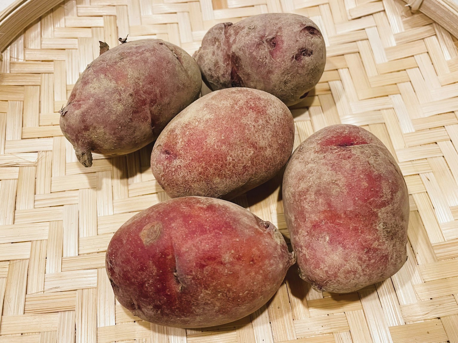 Cinque patate dolci rosse disposte in un cesto di bambù intrecciato