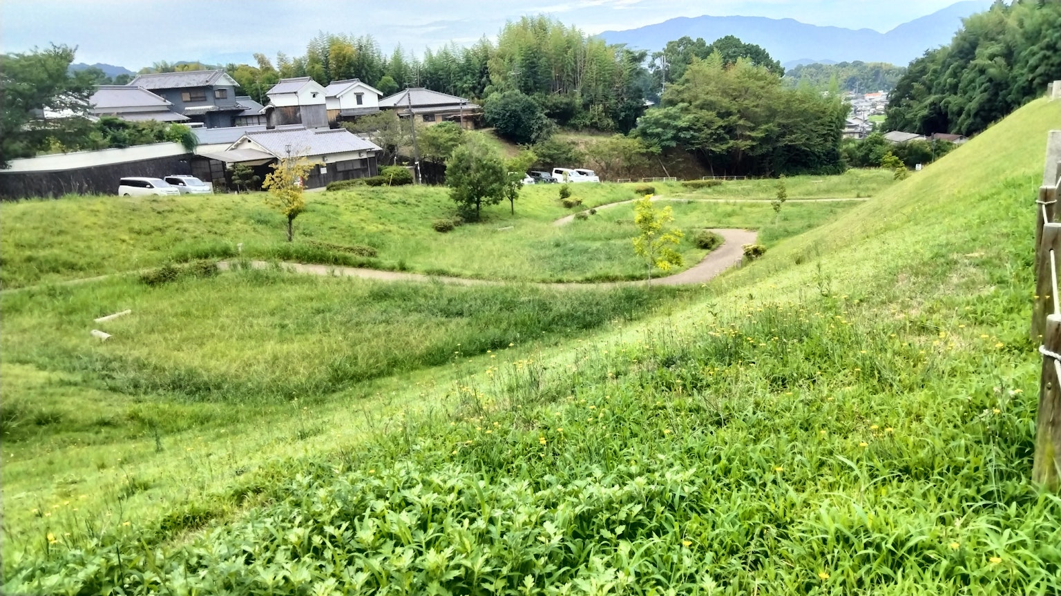 郁郁蔥蔥的山坡景觀，散落著房屋和樹木，草地上的蜿蜒小路