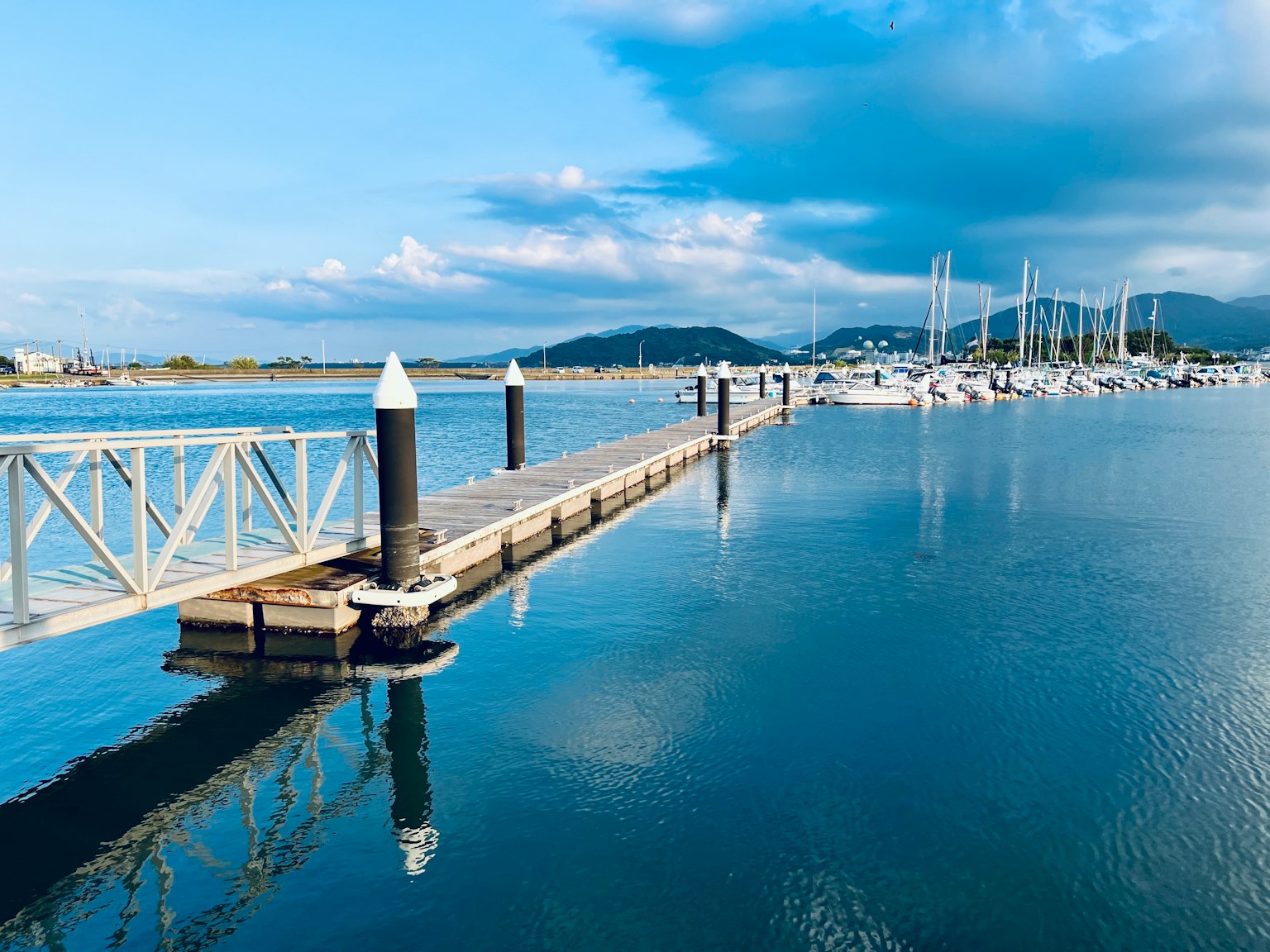 Molo che si estende nell'acqua calma con yacht sullo sfondo