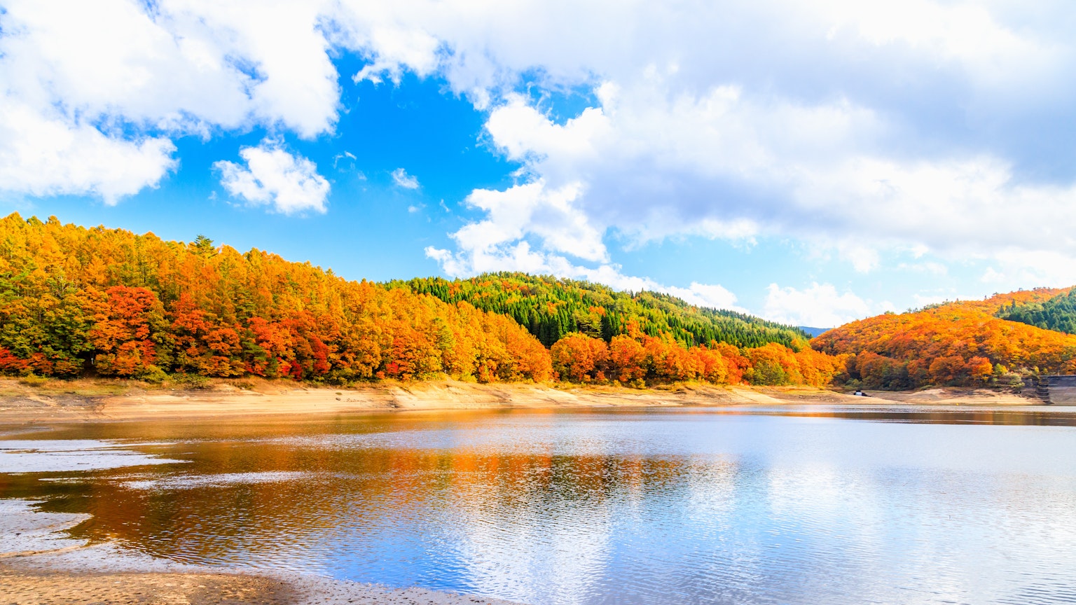 Schöne Herbstlandschaft mit orangefarbenen Bäumen und blauem Himmel, der sich auf einem ruhigen See spiegelt