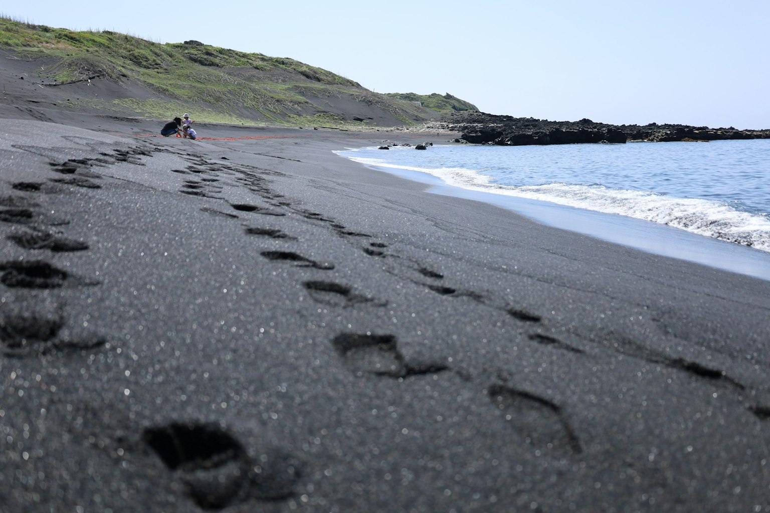 Fußabdrücke an einem schwarzen Sandstrand mit Wellen, die am Ufer brechen