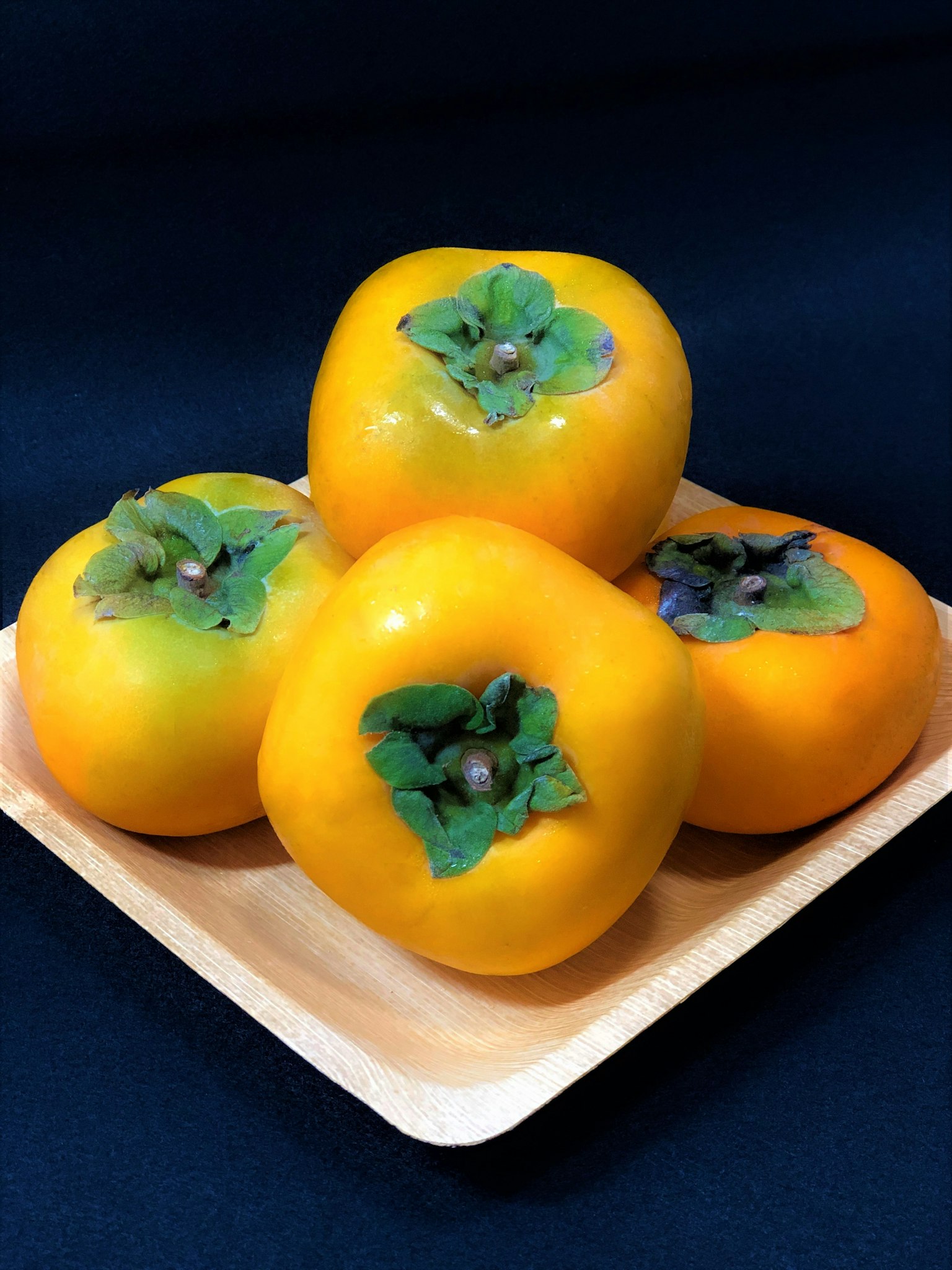 Four yellow persimmons arranged on a wooden plate