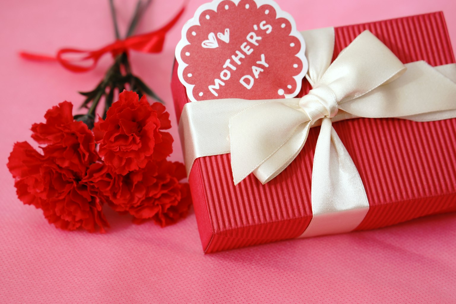 Scatola regalo rossa con etichetta per la festa della mamma e un mazzo di garofani