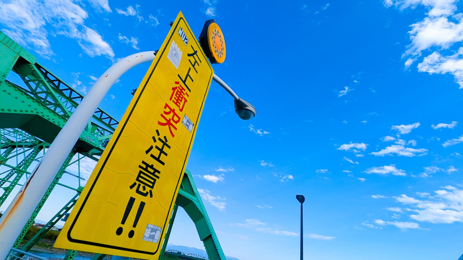 Yellow road sign under blue sky with green bridge structure