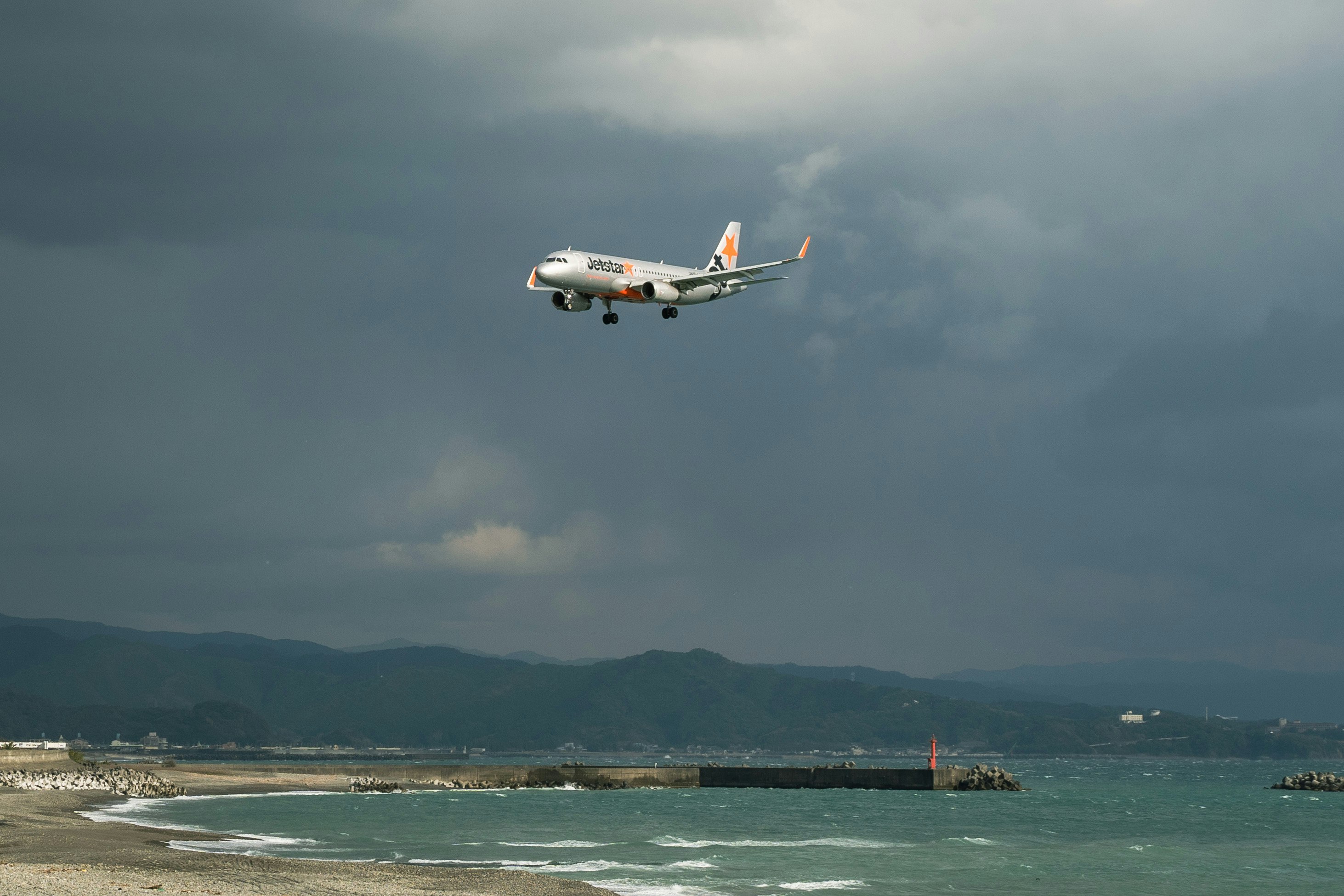 海上を飛ぶ旅客機と港の防波堤のある海岸