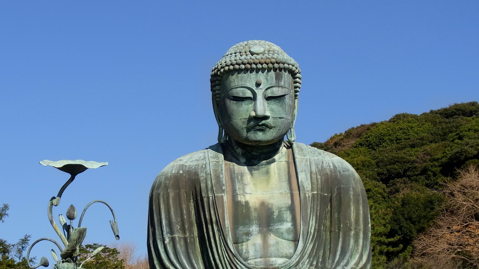 Una statua di Buddha in bronzo sotto un cielo azzurro con espressione serena e dettagli intricati