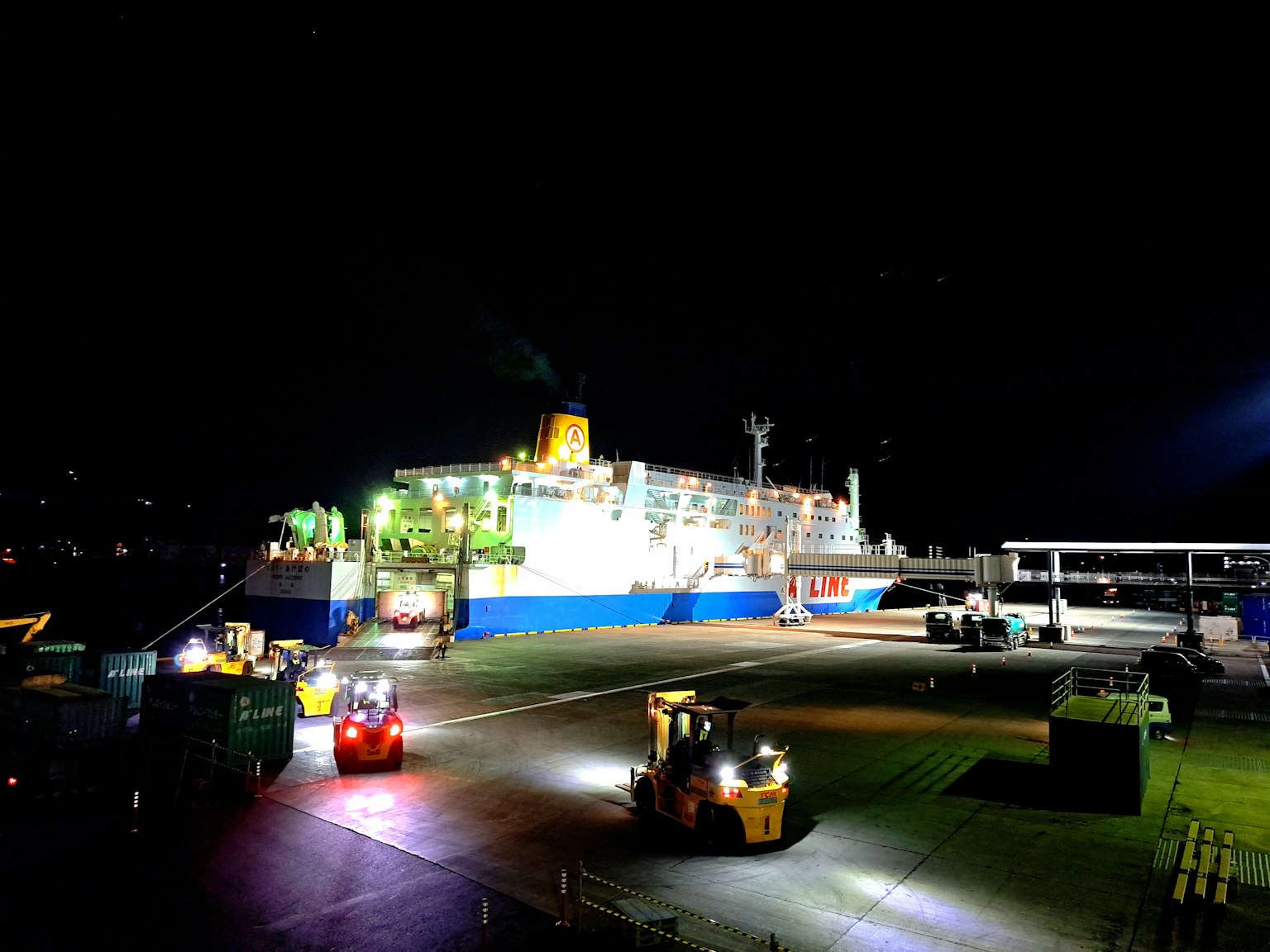 Scena notturna di carrelli elevatori e nave cargo nel porto