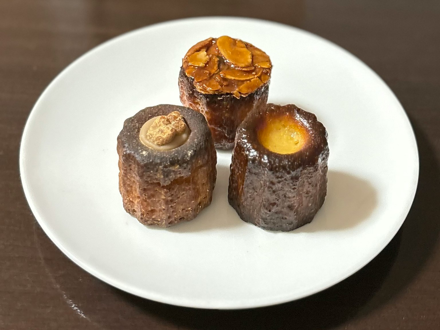 Three baked goods on a white plate featuring one with almond topping and others with creamy textures