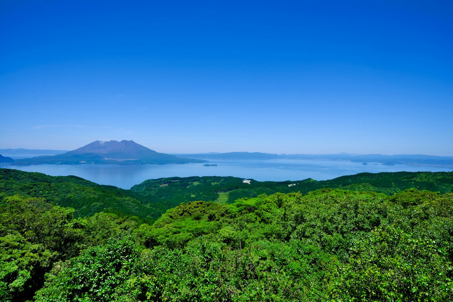 綠意盎然的山丘遠處可見火山在晴朗的藍天下的風景