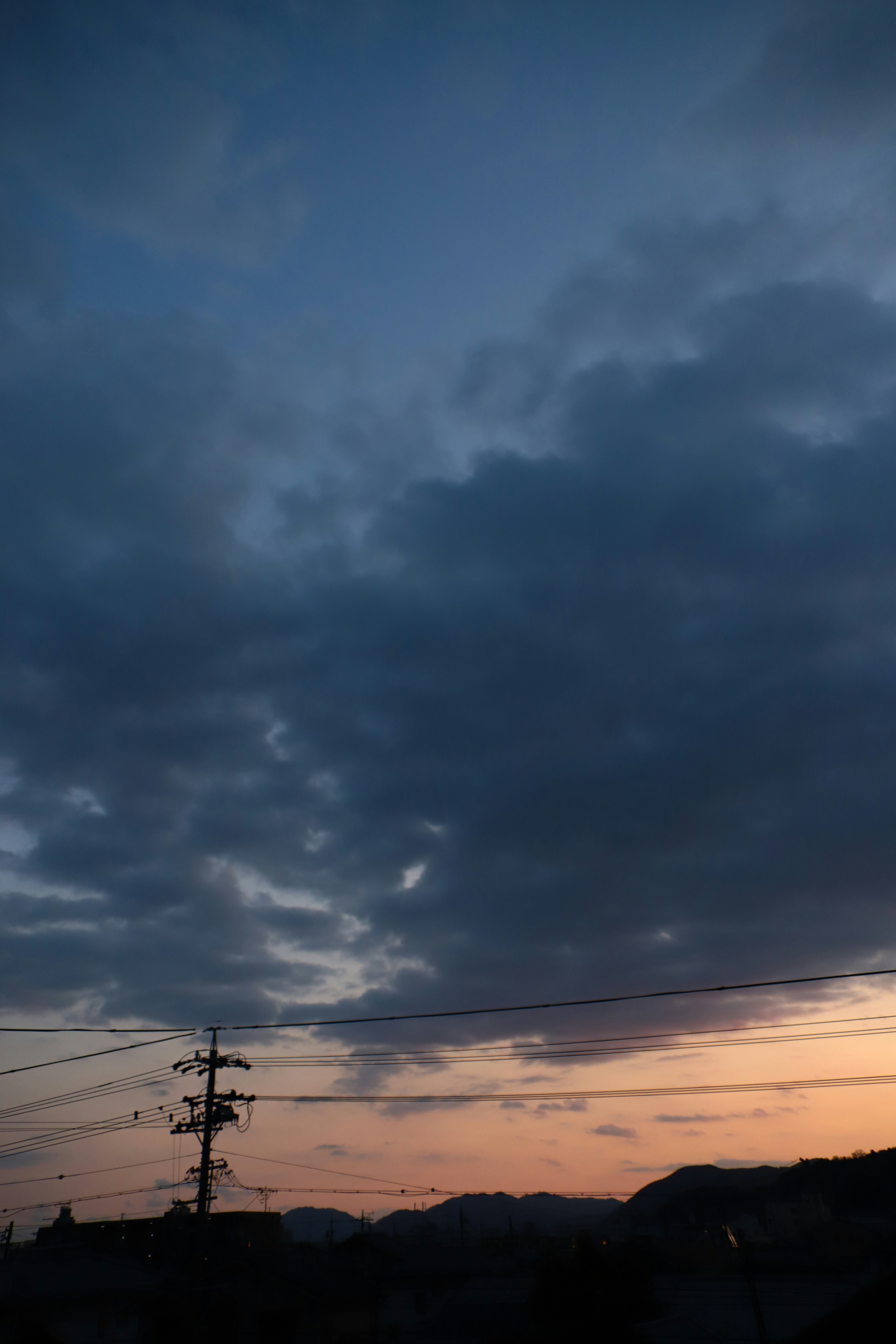 夕焼け前の雲が広がる空と山並みのシルエット