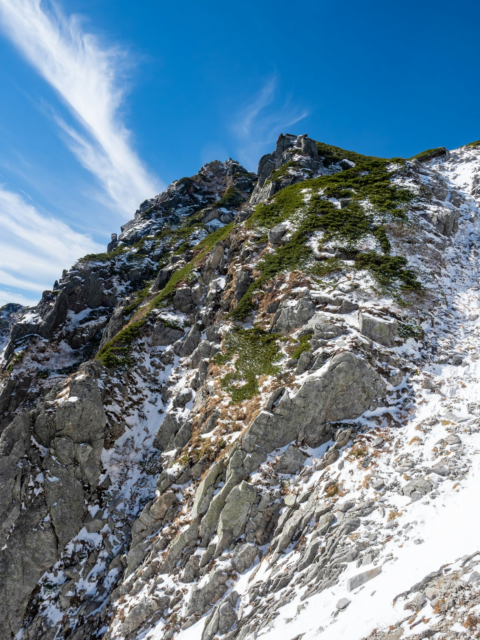Pendiente montañosa rocosa cubierta de nieve bajo un cielo azul claro