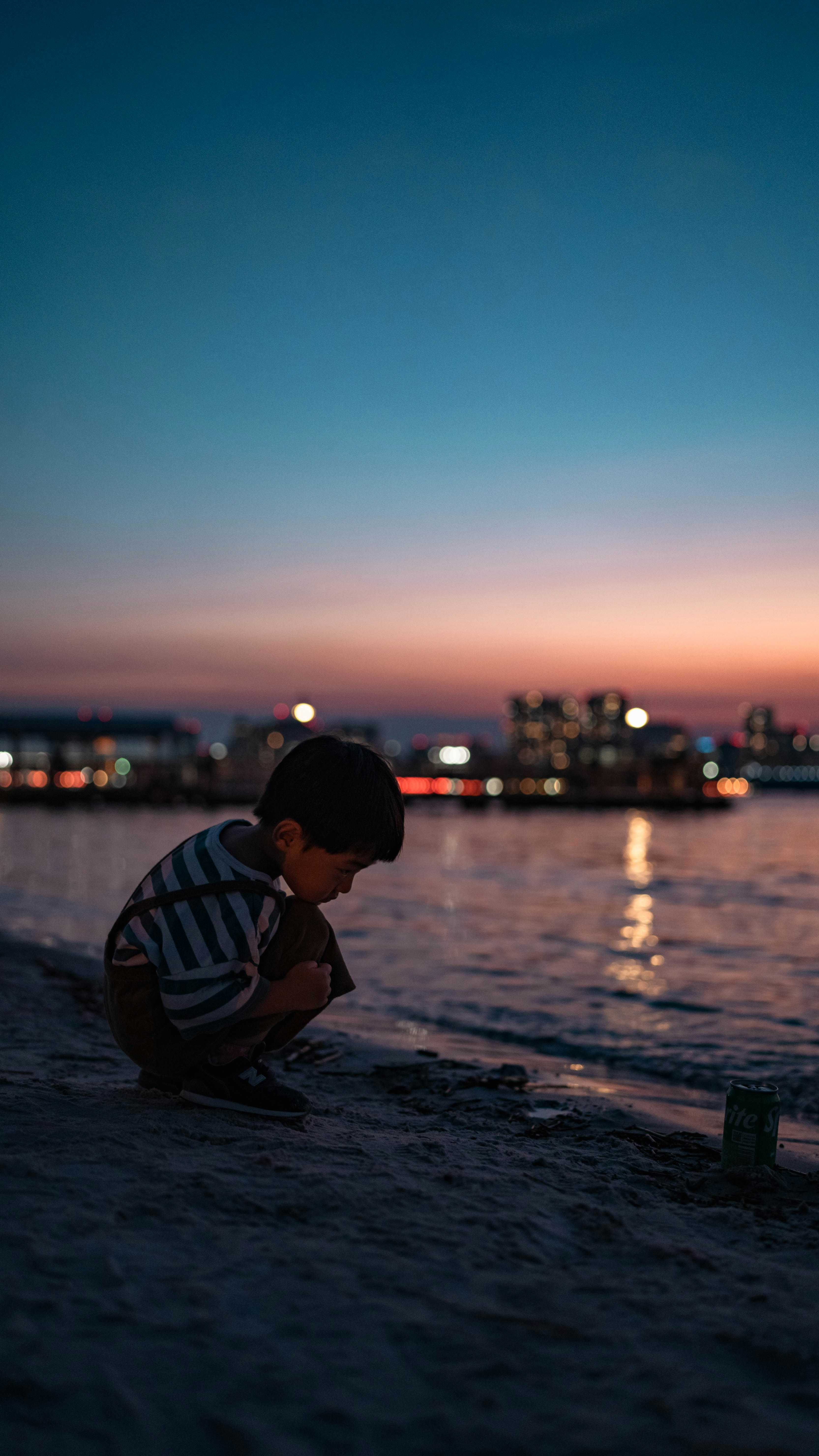 side profile of a child sitting by the seaside at dusk